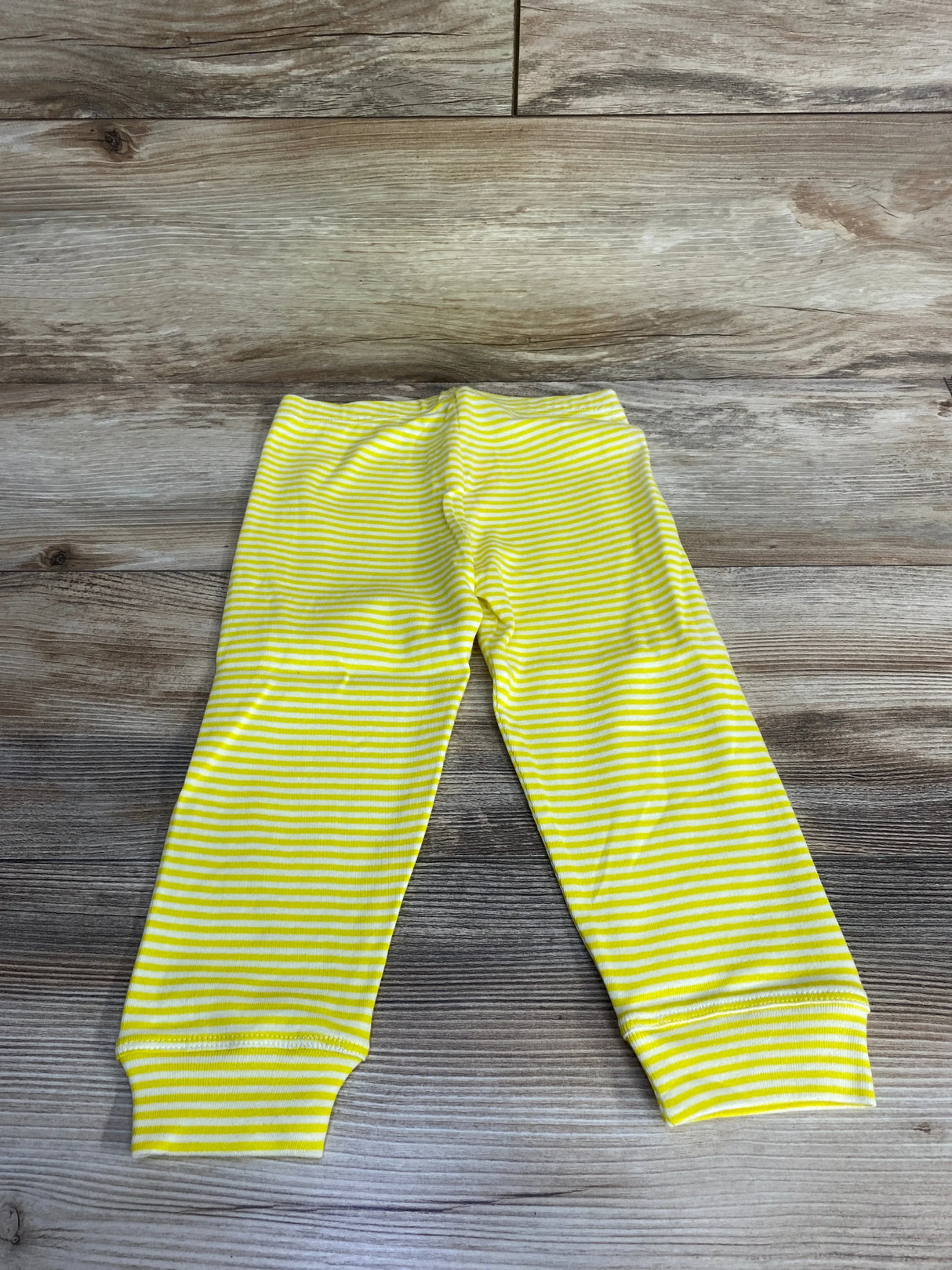 Yellow and white striped soft baby leggings on wooden floor background