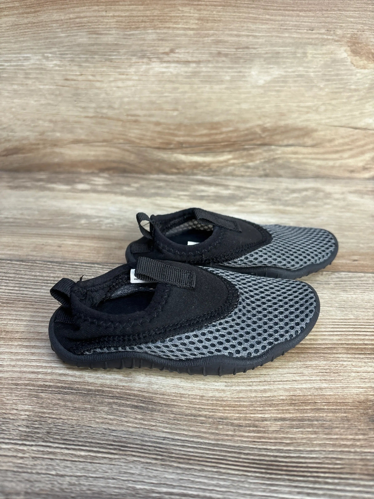 Angled view of Wonder Nation aqua sock water shoes in black and gray with mesh uppers and hook and loop straps on a wood grain floor