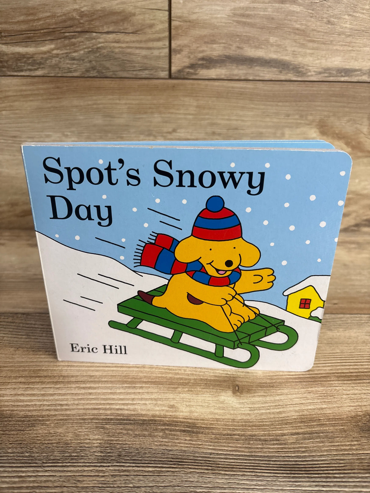 Children's board book Spot's Snowy Day by Eric Hill featuring a dog sledding in snow with winter hat and scarf