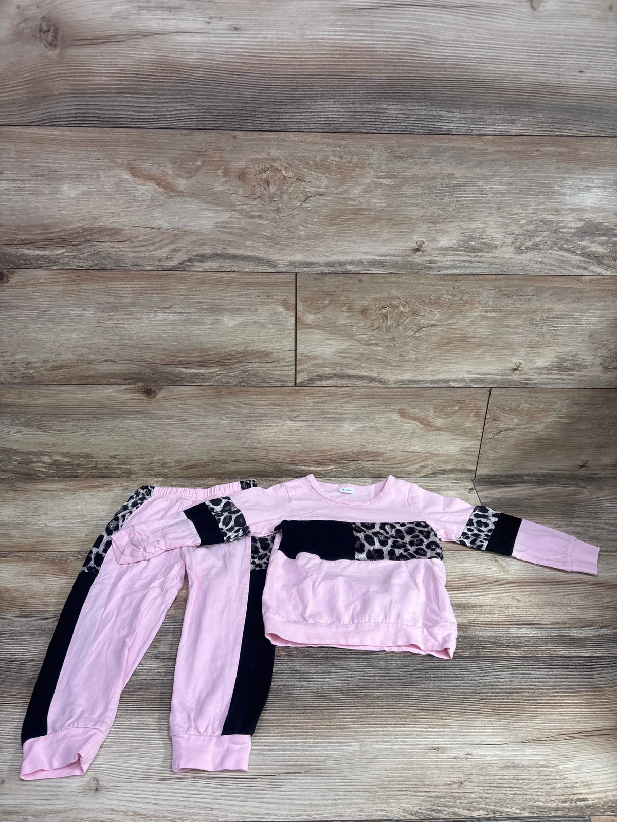 Top view of pink 2-piece leopard color block sweatshirt and joggers set showcasing black panels with a wood plank background