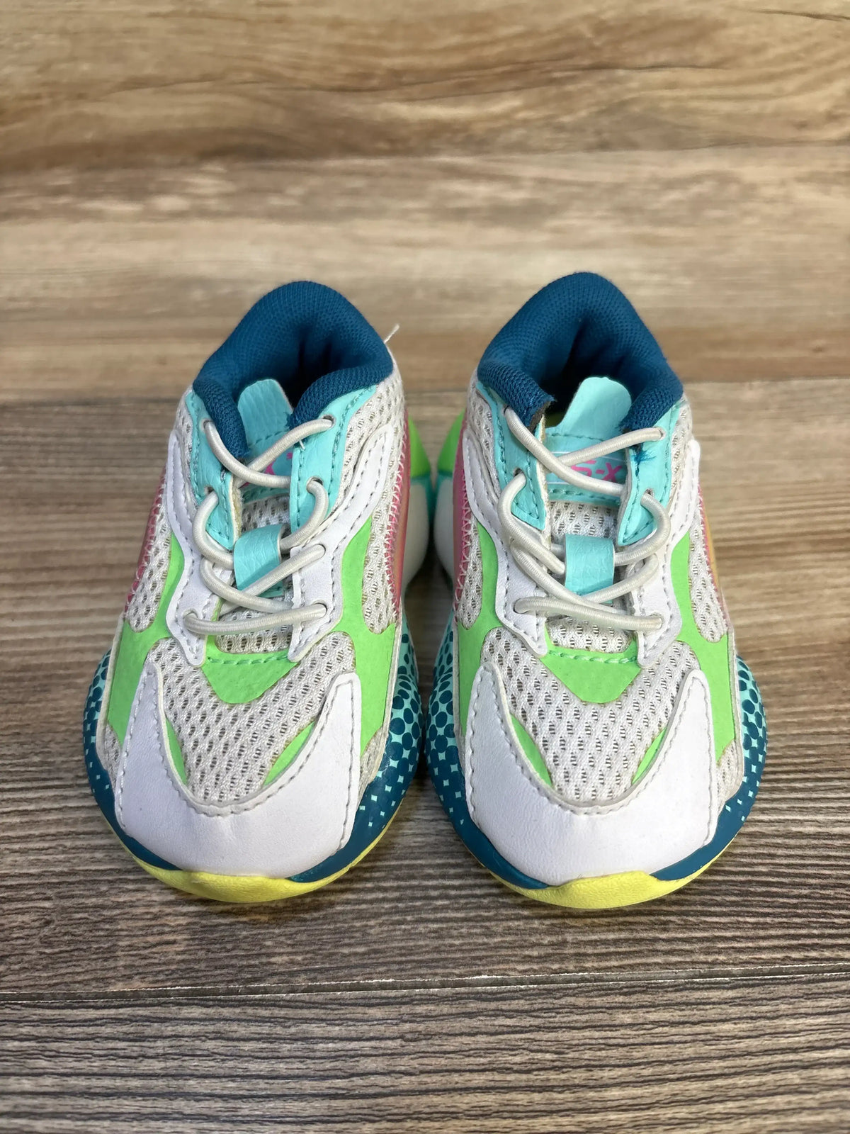 Front view of Puma RS-X3 WR toddler sneakers, white with green and teal accents, mesh upper and elastic laces on wooden floor