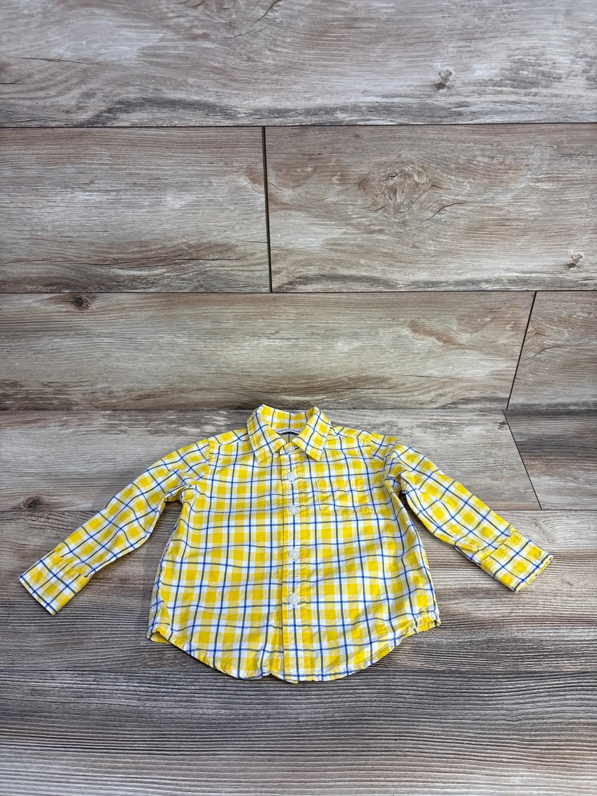 Front view of Janie & Jack yellow plaid shirt, size 12-18m, with long sleeves, collar, and breast pocket on wood background