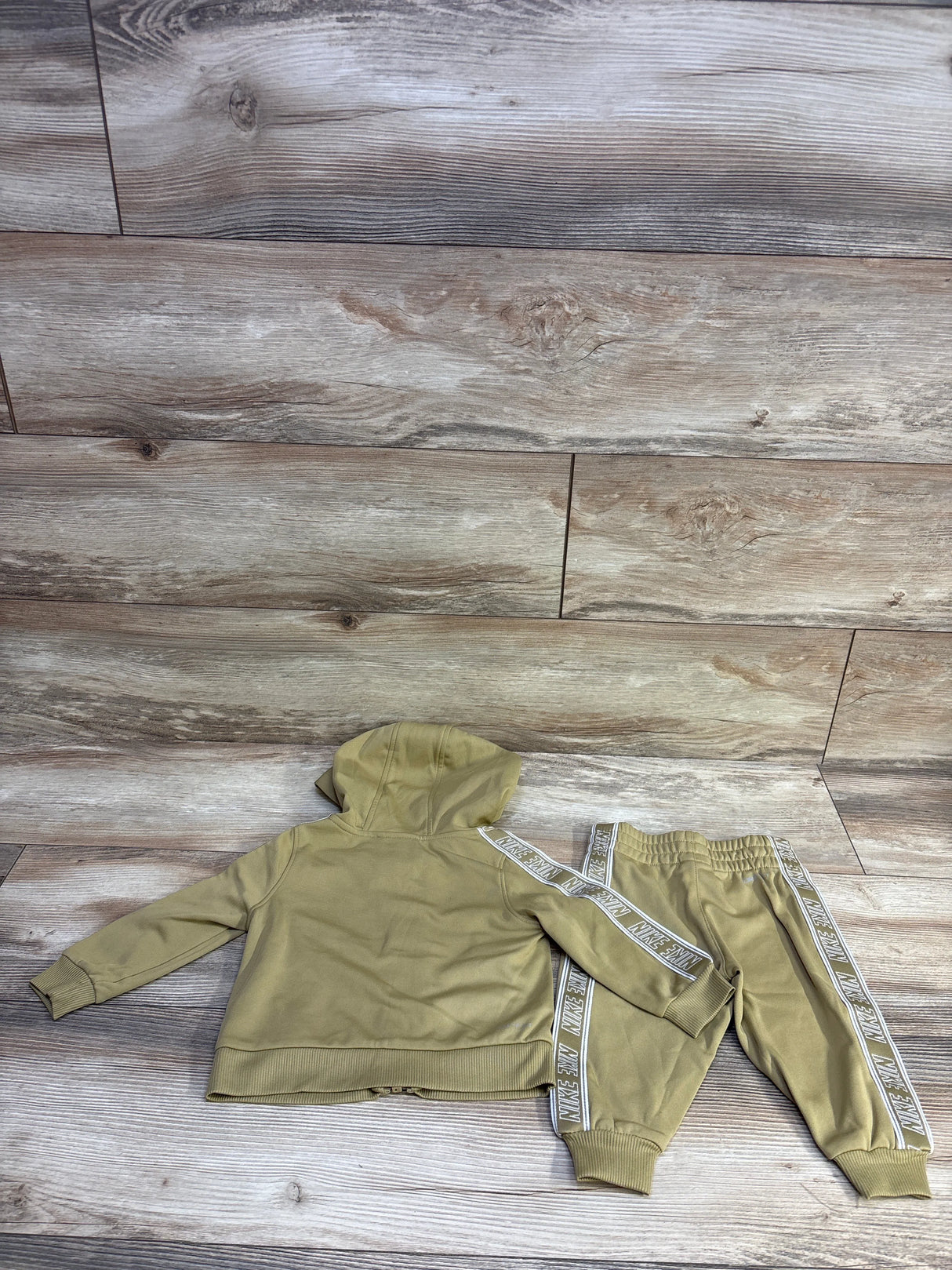 Flat lay of tan Nike 2-piece Dri-Fit tracksuit 12M showing hooded zip top and joggers with Nike side tape on wood