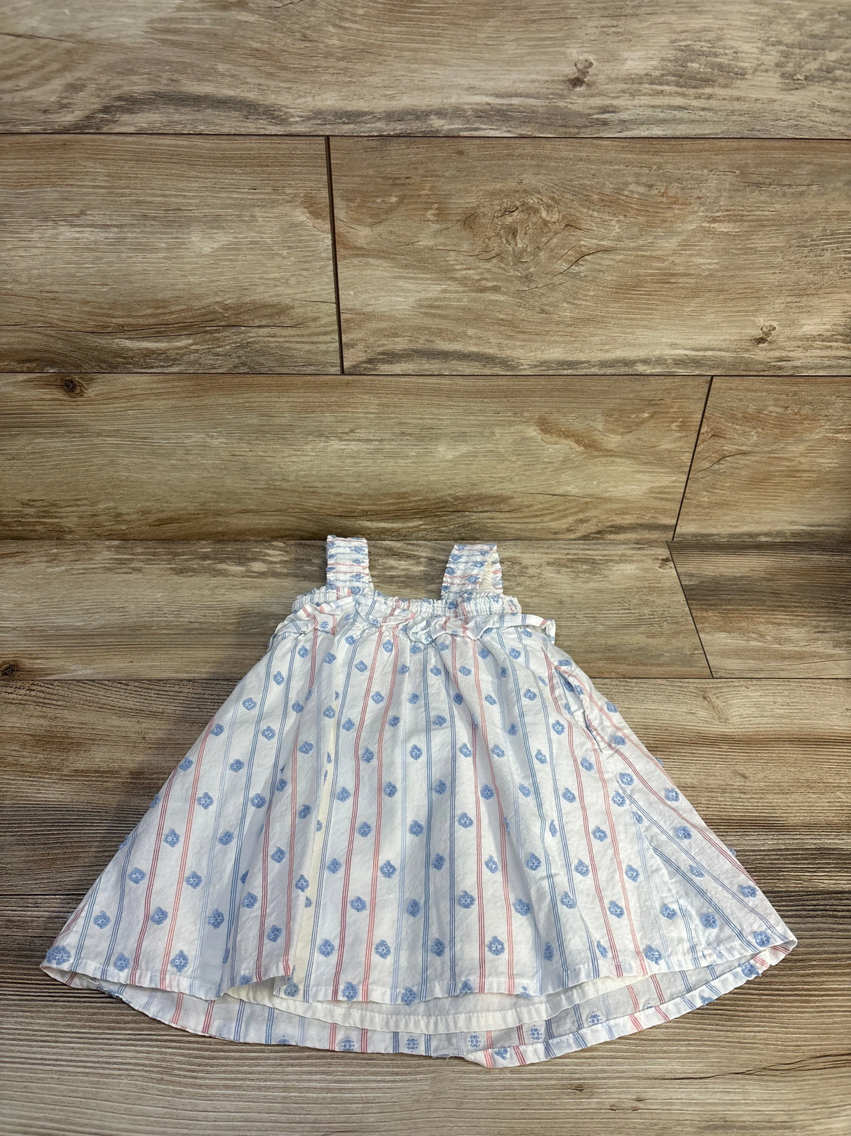 Baby girl's striped floral dress with smocked bodice, laid on wood floor for resale