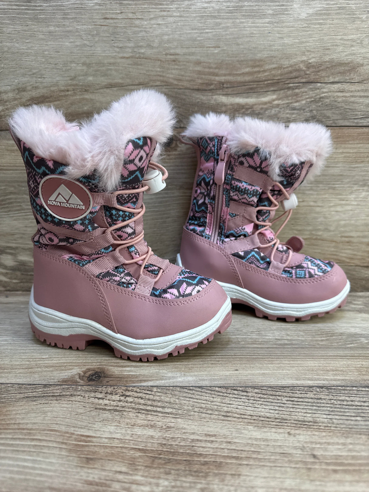 Side view of pink Nova Mountain snow boots with faux-fur cuff, patterned knit upper, side zipper and rugged sole on wood