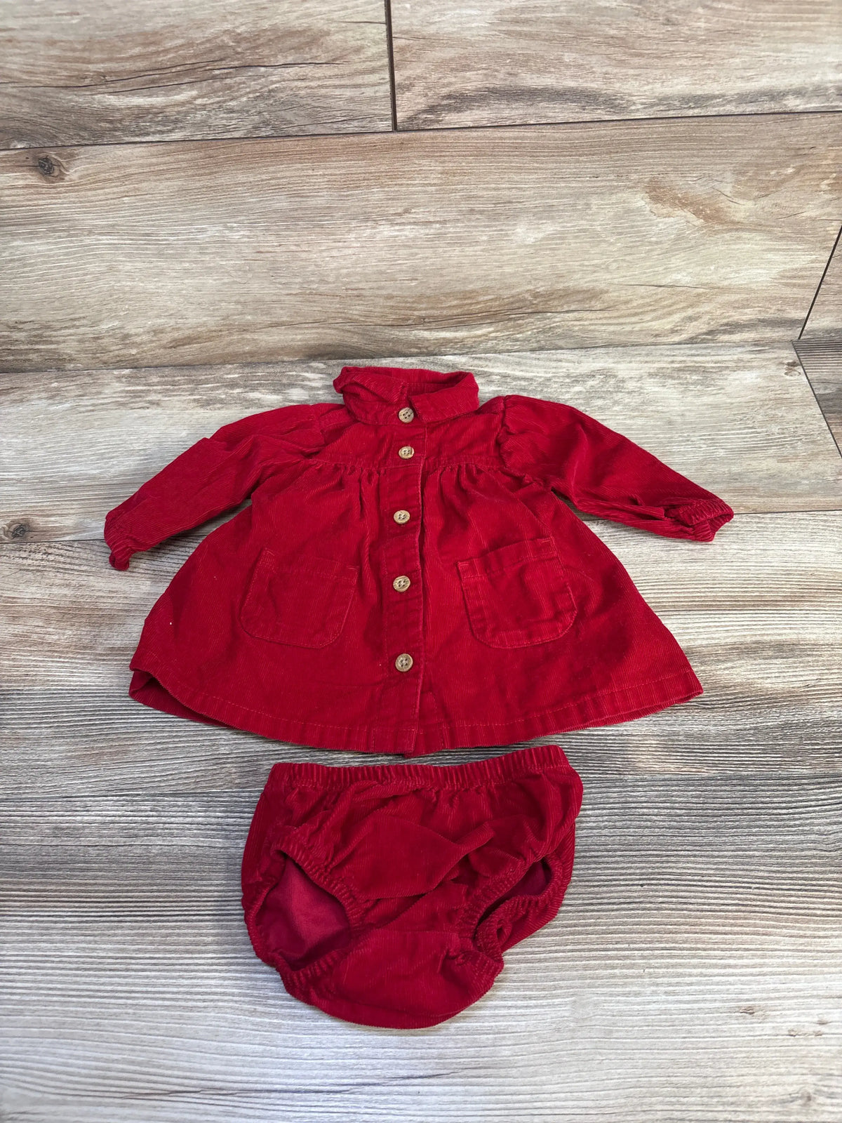 Front view of Carter’s newborn red corduroy dress and bloomers set showcasing button front closure with wood flooring