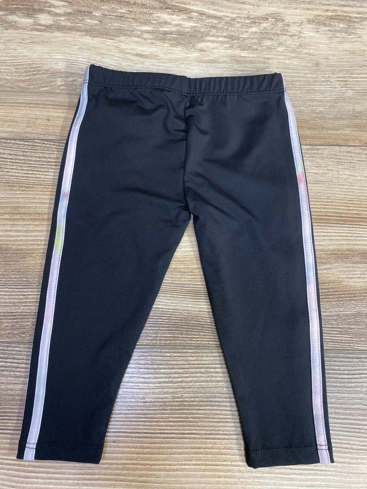 Black leggings with pastel rainbow side stripes laid on wooden floor
