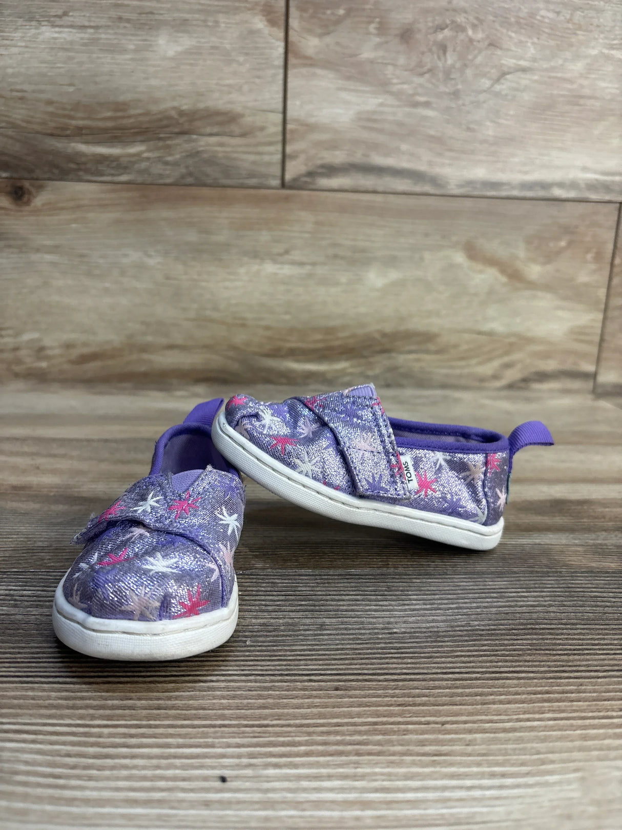 Purple glitter toddler shoes with star pattern, slip-on design, white soles on wood floor