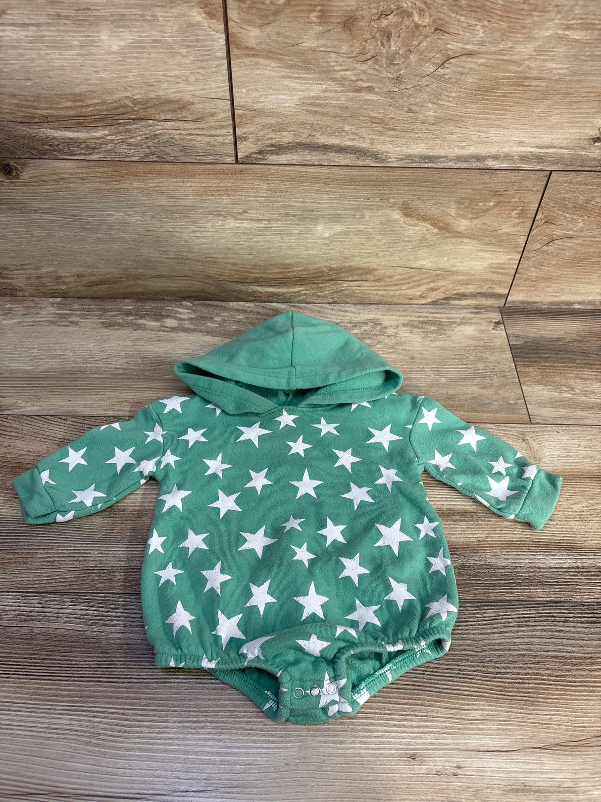 Front view of Grayson Mini star print hooded sweater romper in green showcasing its hood and snap closures on a wood floor