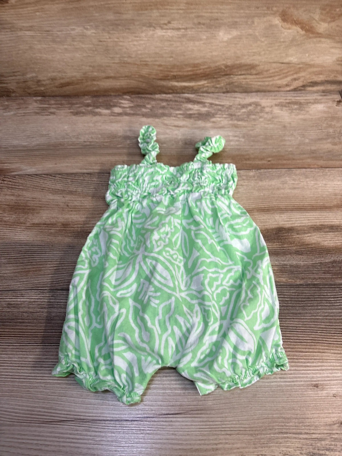 Front view of Carter’s green tank shortie romper showcasing its white abstract pattern and elastic leg openings on a wood surface
