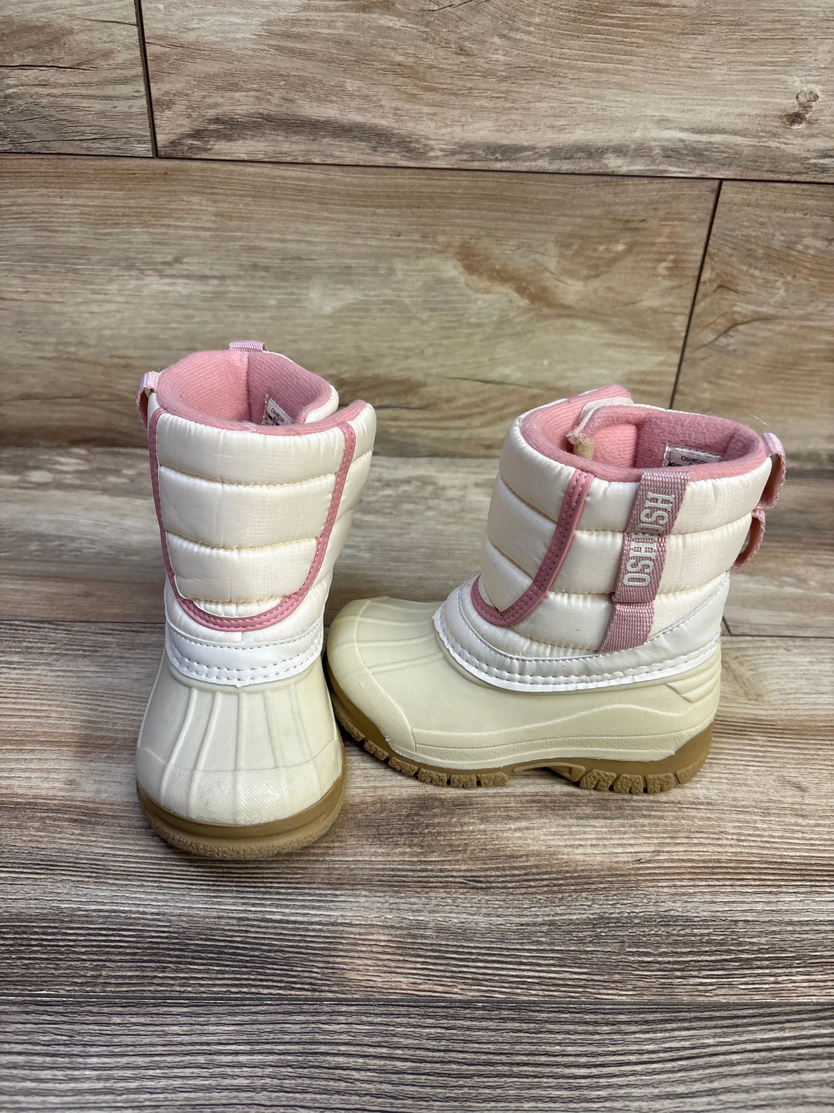 Front and side view of Oshkosh Splash kids winter boots in ivory with pink trim, rubber sole on wood floor