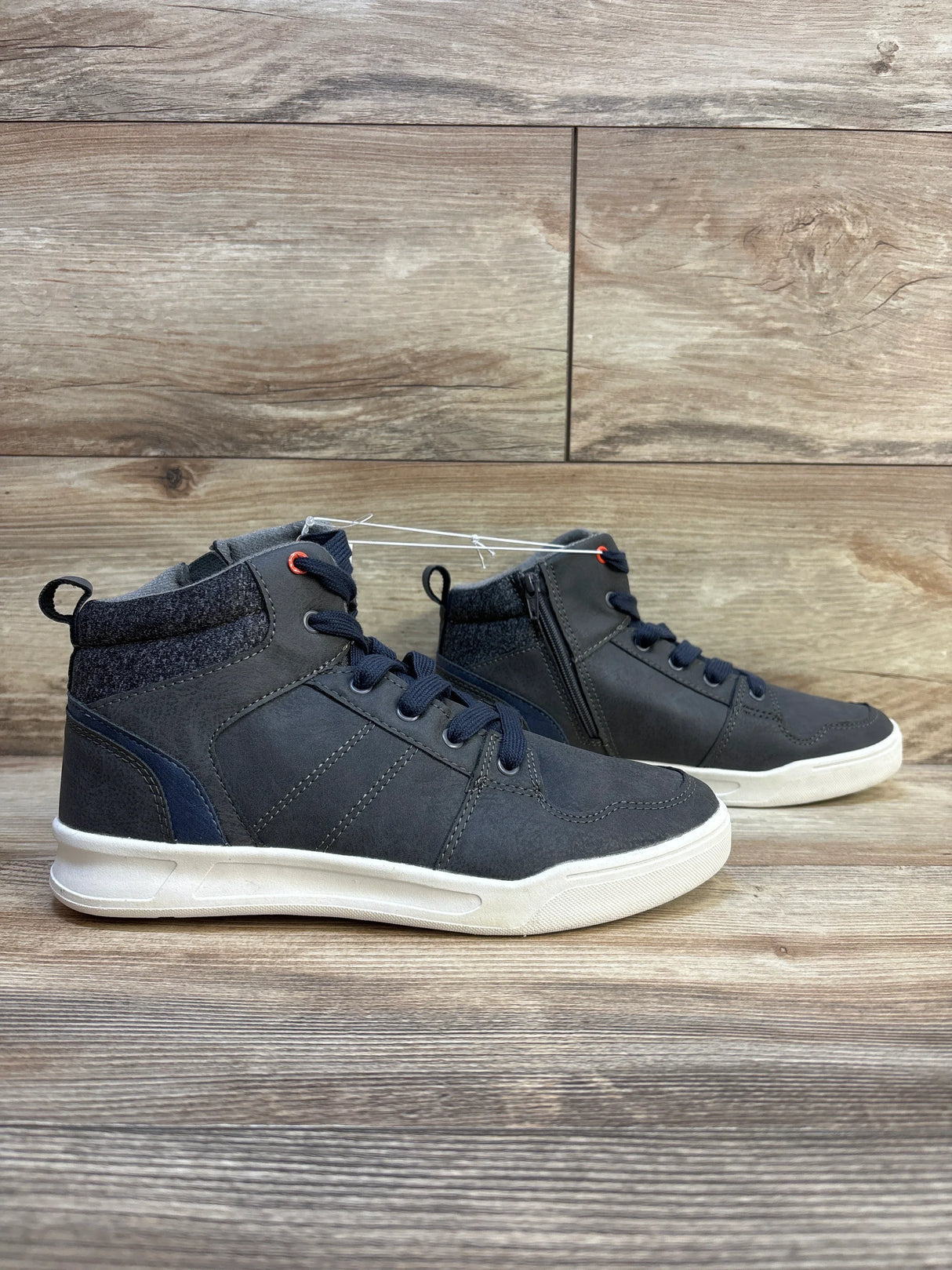 Side view of Art Class Geoff high-top kids sneakers in grey showing lace-up front, side zipper, and white soles on wood floor