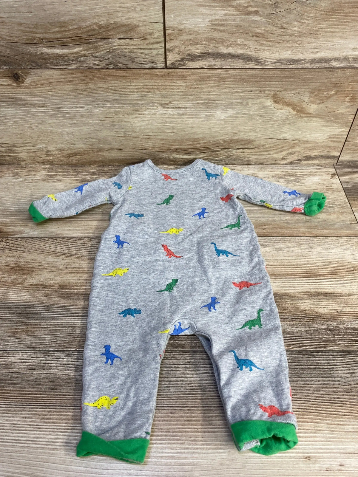 Gray baby onesie with colorful dinosaur prints and green cuffs laid flat on wood floor