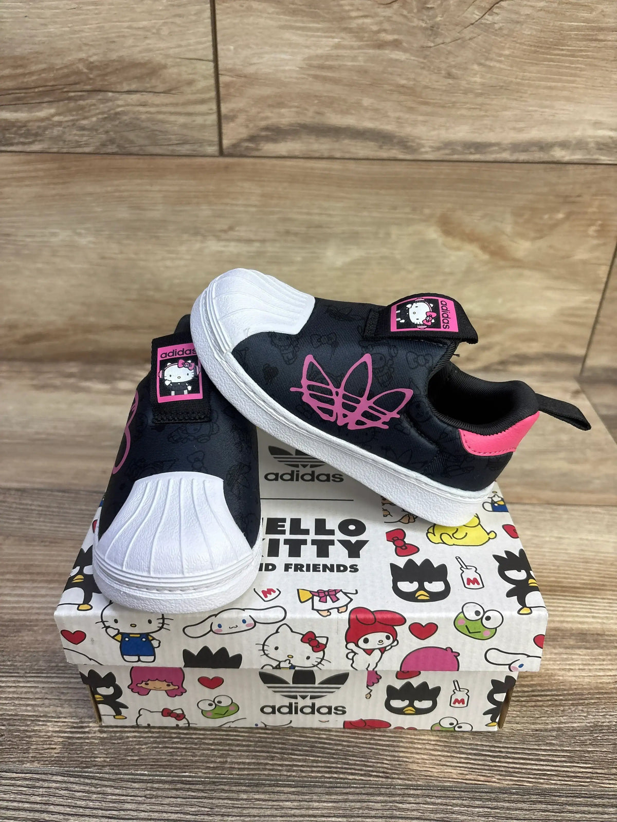 Angled view of Adidas x Hello Kitty Superstar 360 sneakers showing white shell toe and pink logo on Hello Kitty shoebox
