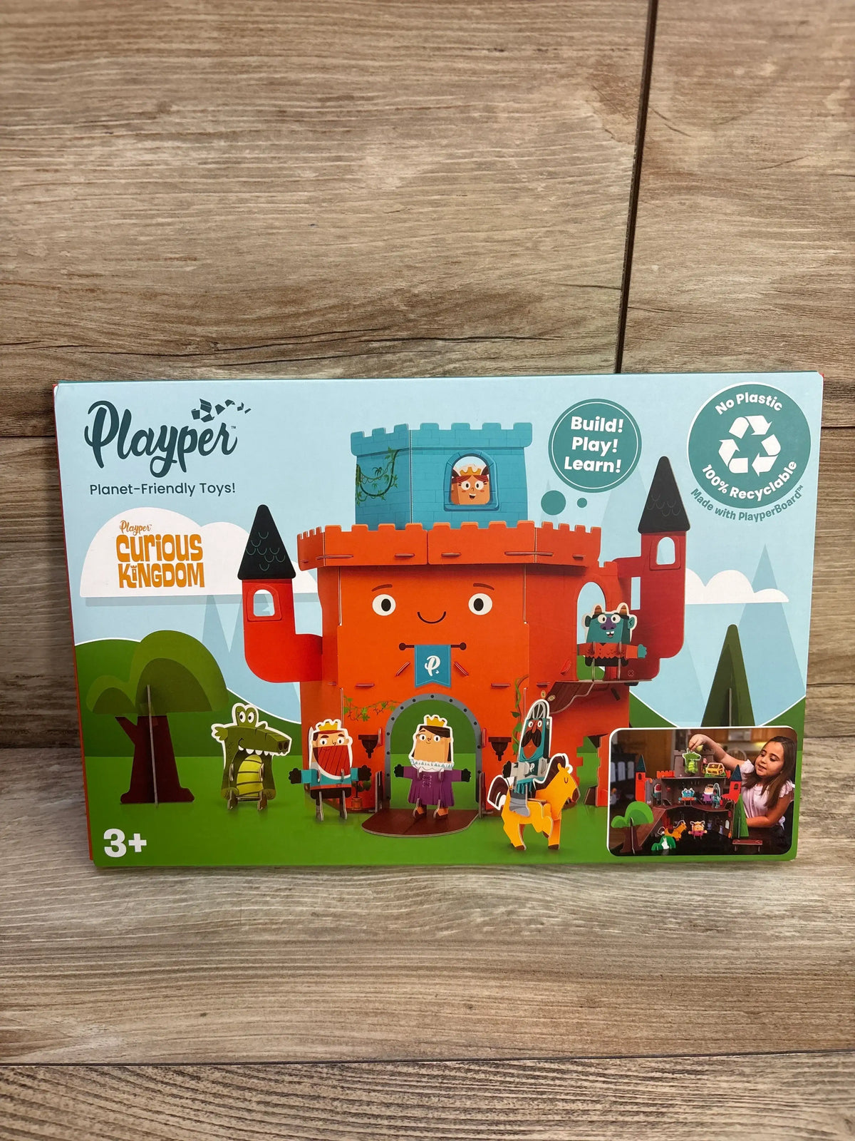 Front view of Playper Curious Kingdom castle box showing assembled colorful castle with figures on wooden background