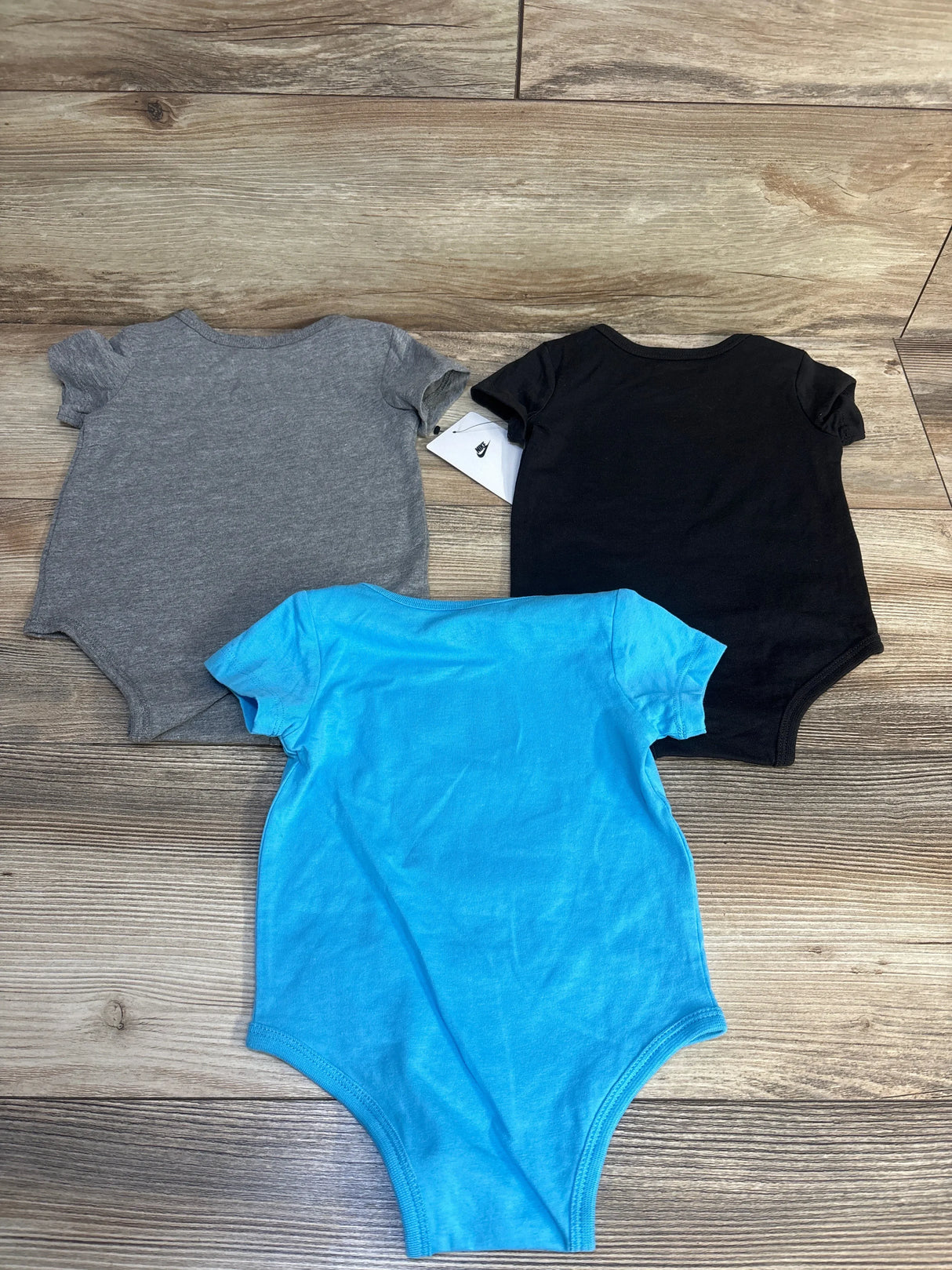 Three short sleeve baby bodysuits in gray, black, and blue on wood floor