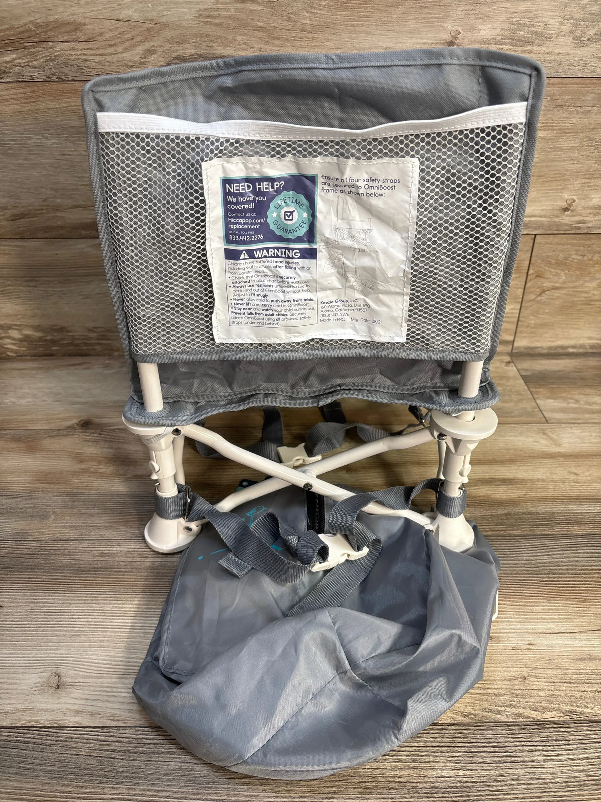 Rear view of gray Hiccapop OmniBoost Folding Booster Chair showing mesh rear pocket and carry bag on wood floor