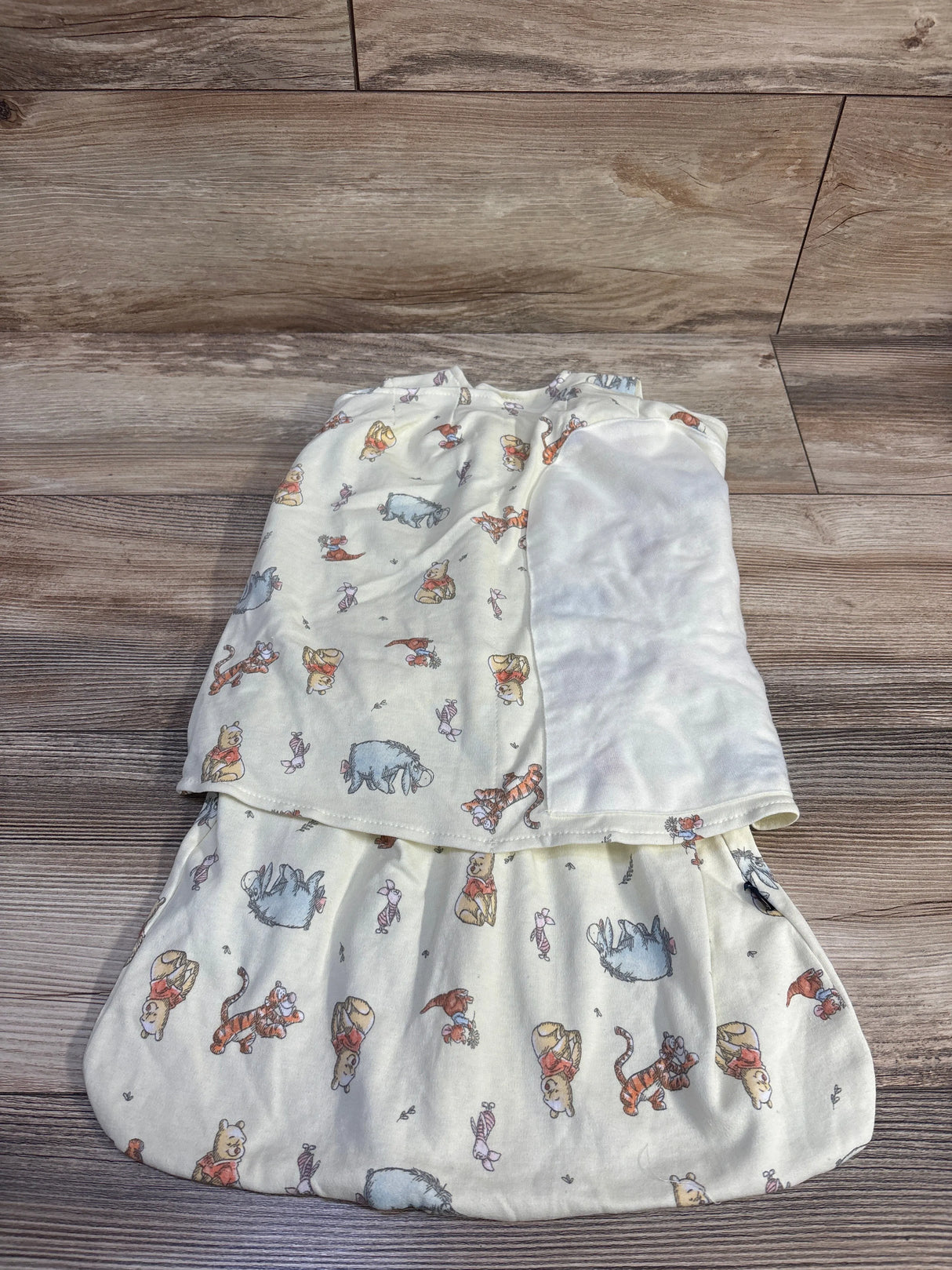 Flat lay of Halo x Disney Winnie the Pooh newborn swaddle showing all-over character print and velour lining on wood floor