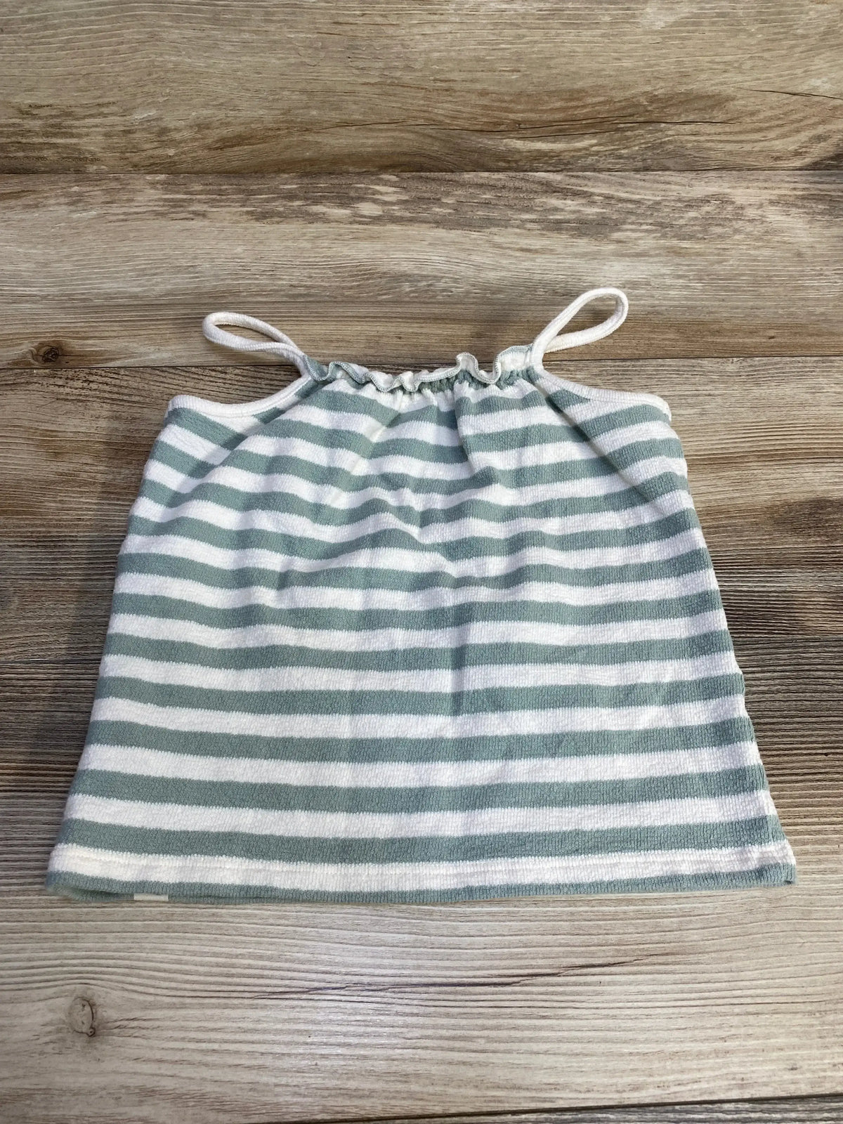 Flat lay of toddler green and white striped tank top showing gathered elastic neckline and thin shoulder straps on wooden surface