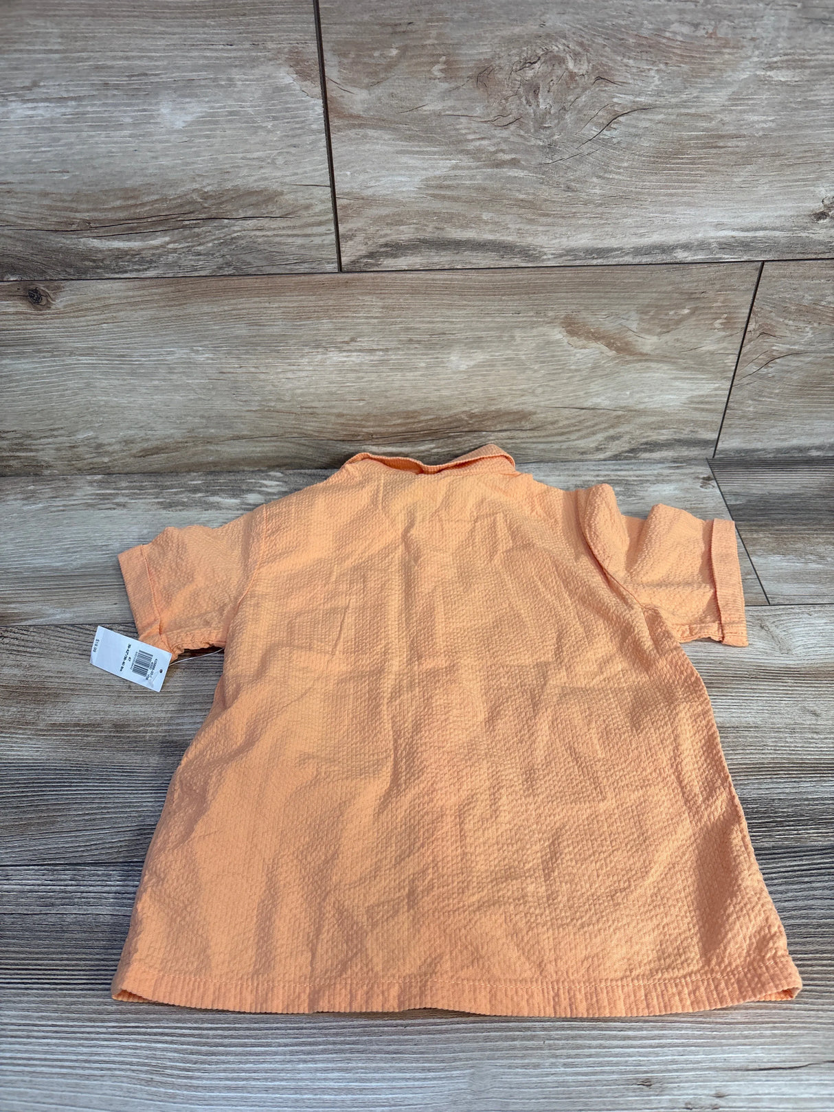 Back view of orange Old Navy crinkle gauze button up toddler shirt showing short sleeves and textured fabric on wood floor