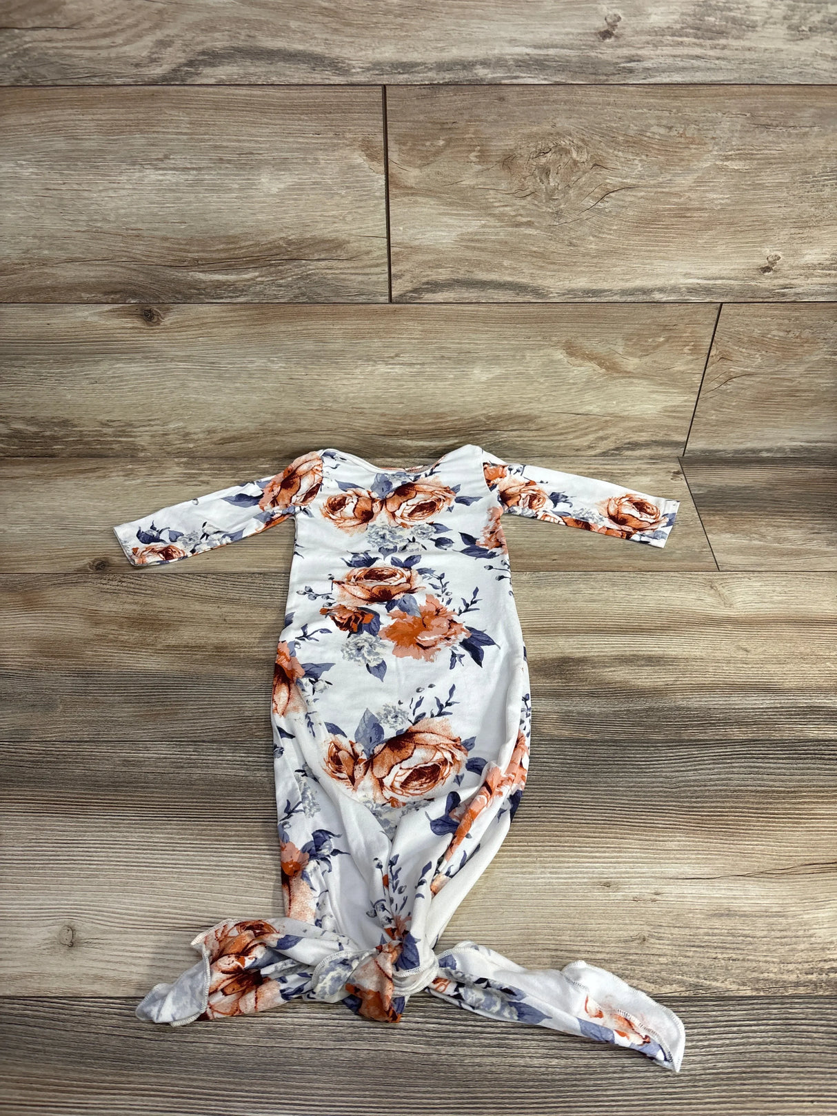 White baby gown with orange and blue floral print laid flat on wooden background for children's resale