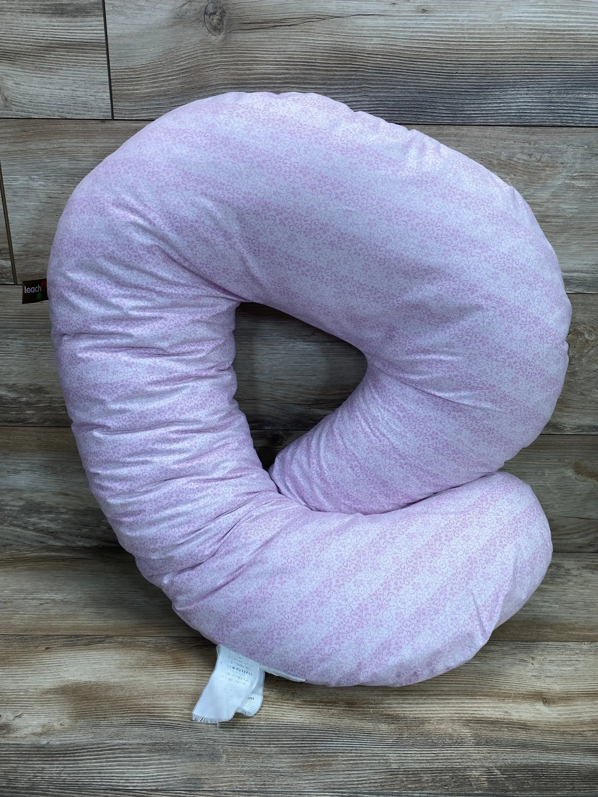 Front view of Leachco Snoogle Mini C-shaped nursing support pillow showcasing light purple microfloral cover on wood plank floor background