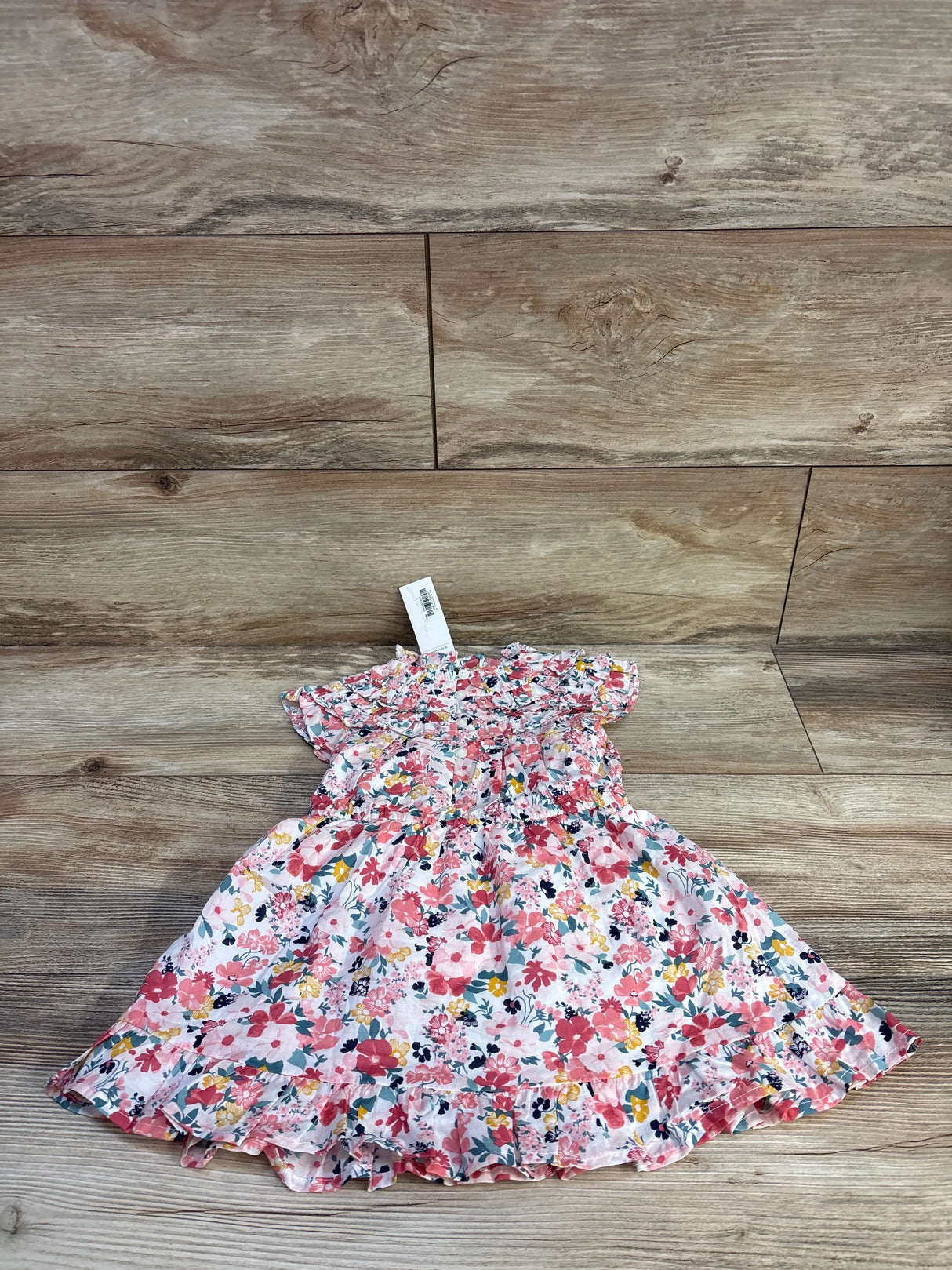 Flat lay of Janie and Jack pink floral dress and bloomers showing smocked bodice and ruffle trim on wood plank background