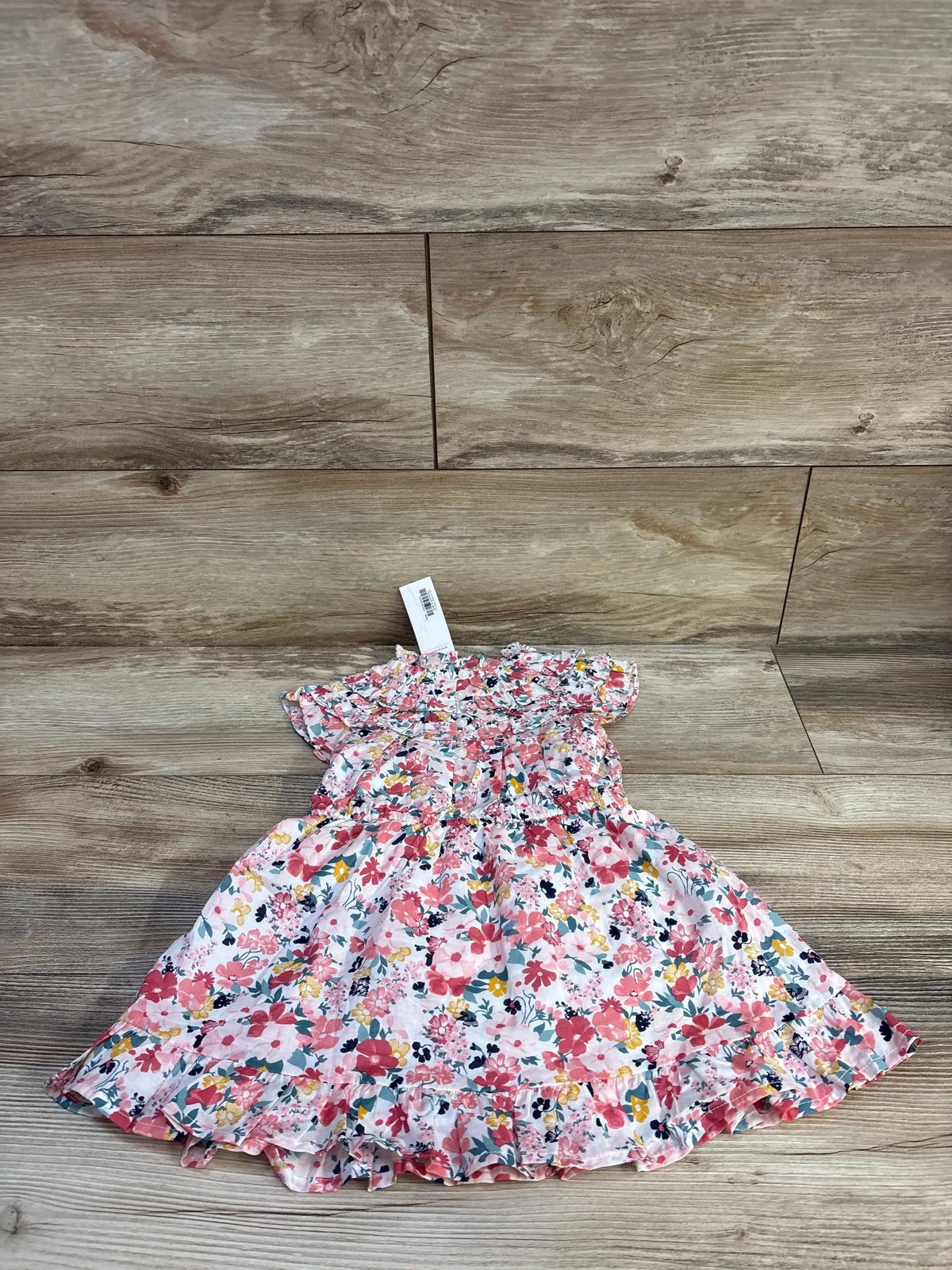 Flat lay of Janie and Jack pink floral dress and bloomers showing smocked bodice and ruffle trim on wood plank background