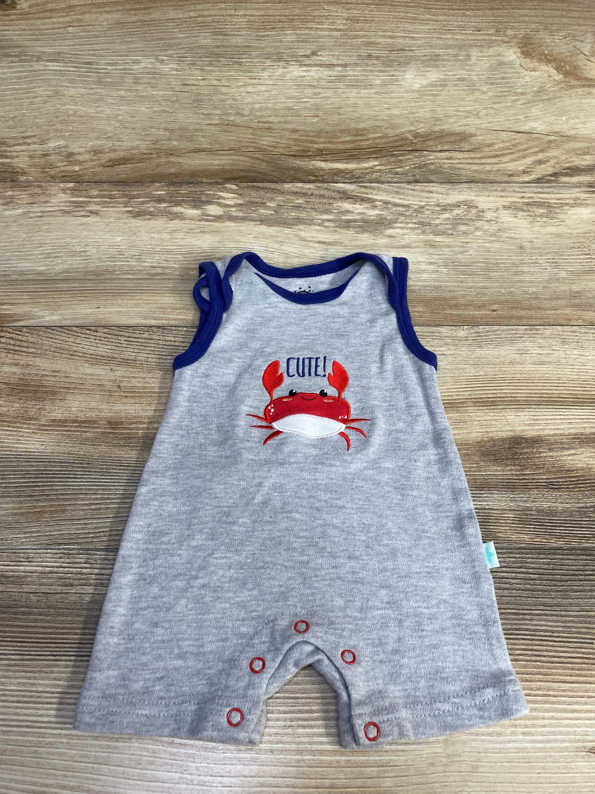 Flat lay of grey Millie & Myles shortie romper with navy trim, embroidered red crab and CUTE! text, sleeveless, snap crotch on wood