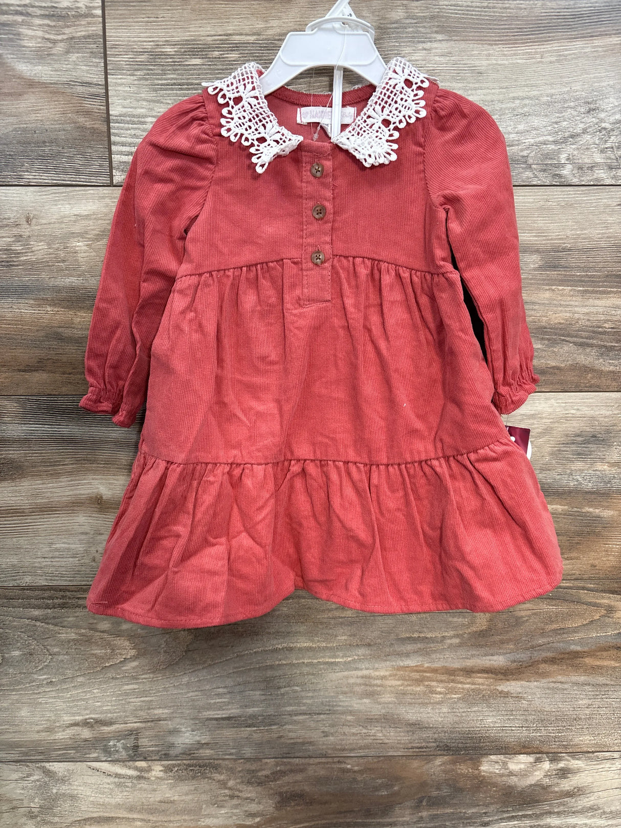 Coral pink corduroy toddler dress with lace collar and brown buttons, displayed on wooden floor