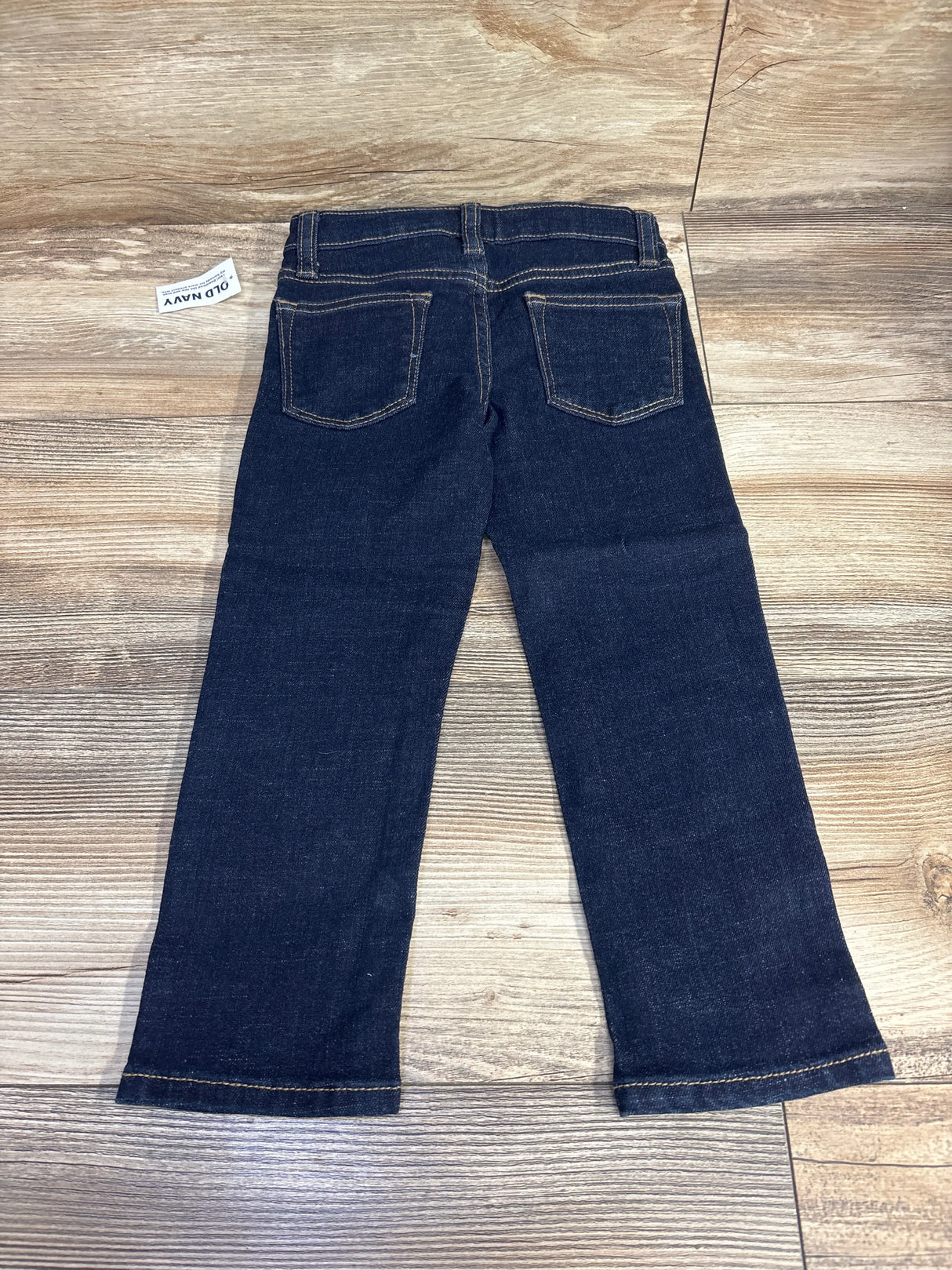 Dark wash kids denim jeans with back pockets, laid flat on wood floor