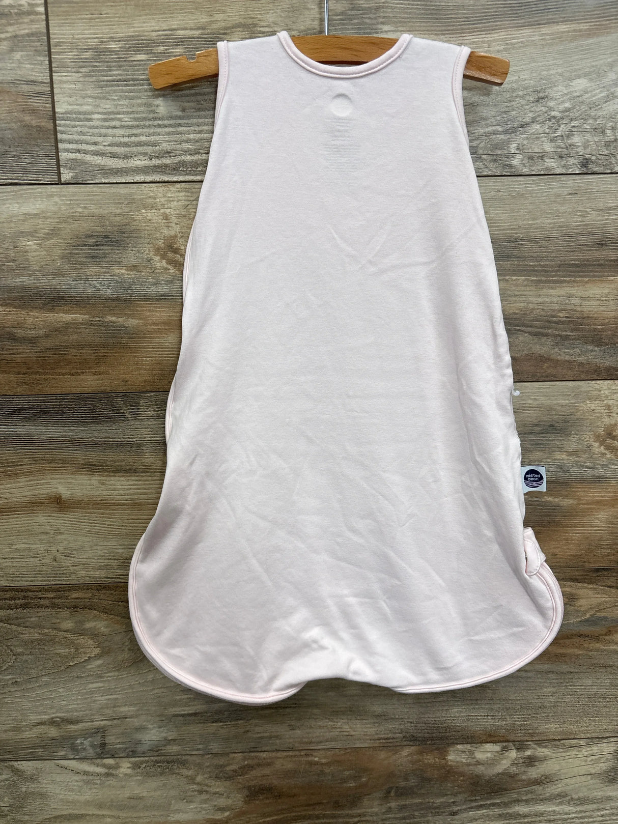 Light pink sleeveless baby sleep sack on wooden hanger, wood background