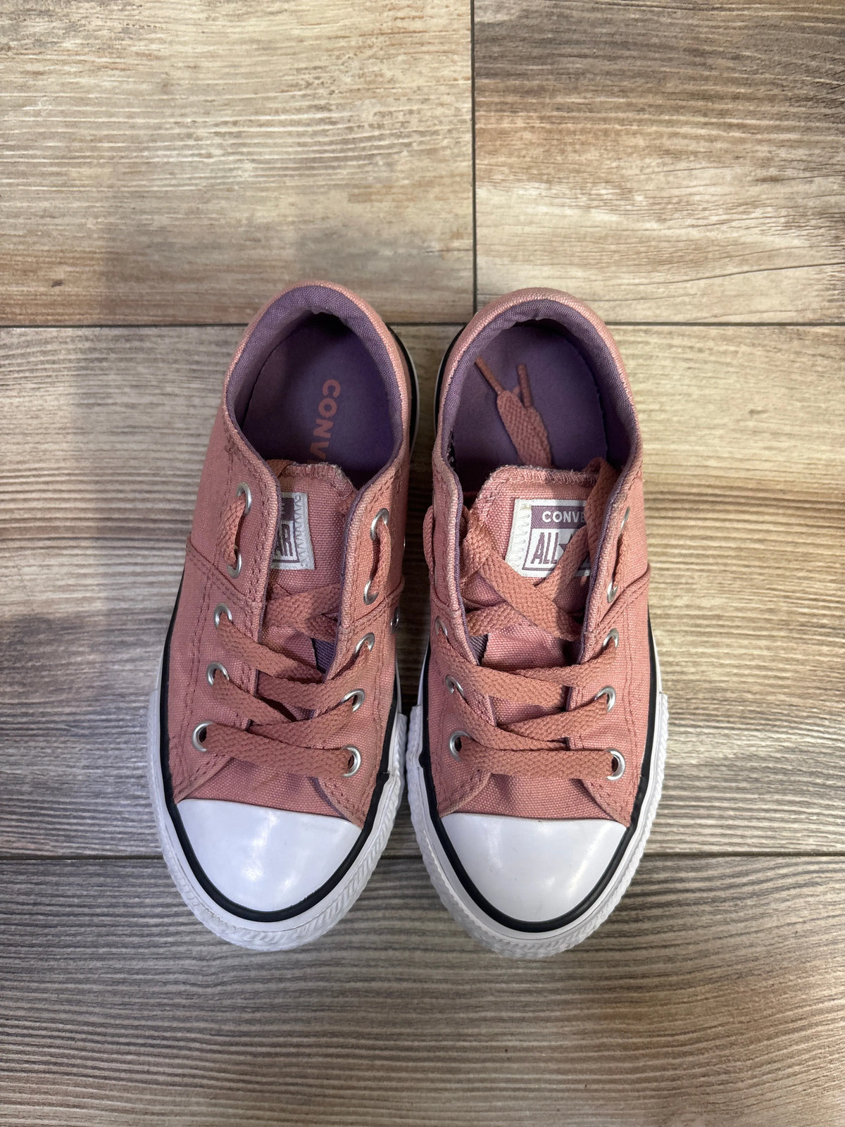 Top view of Converse Chuck Taylor All Star Maddison sneakers showcasing pink uppers, white toe caps, and laces on a wood surface