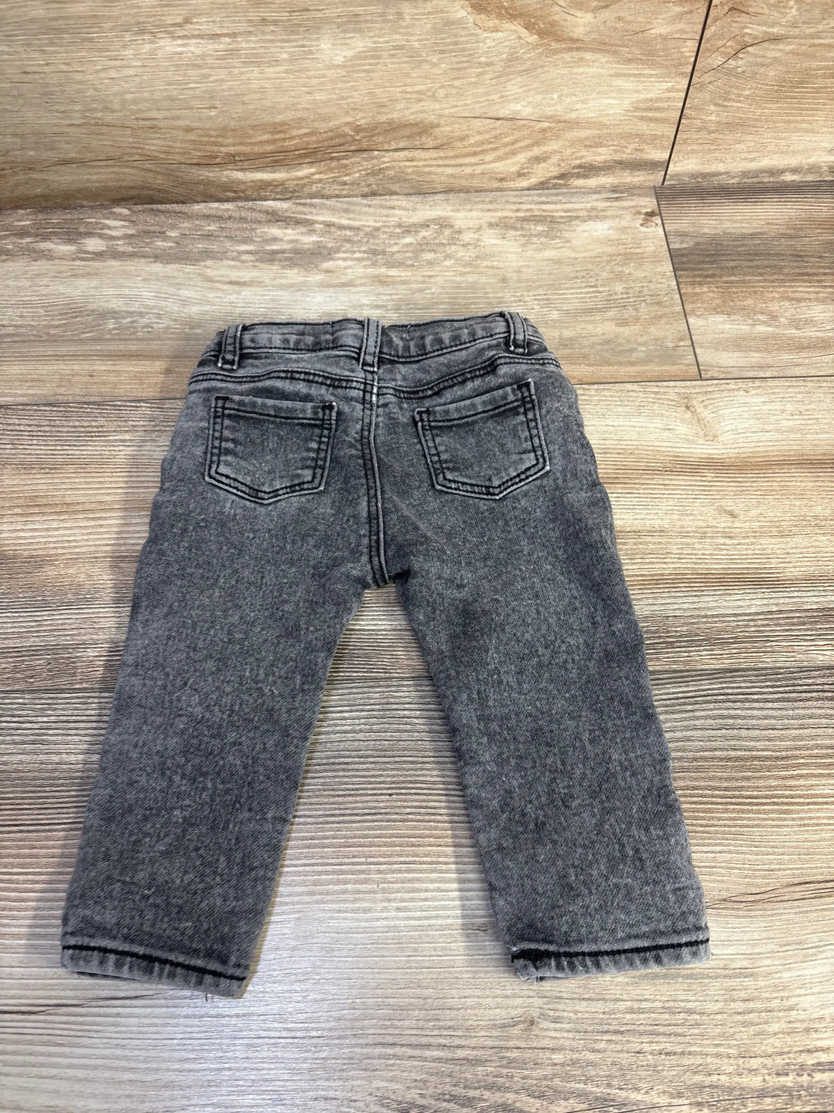 Rear view of Cotton On baby jeans in grey, size 6-12 months, showcasing two back pockets on a wood-look floor