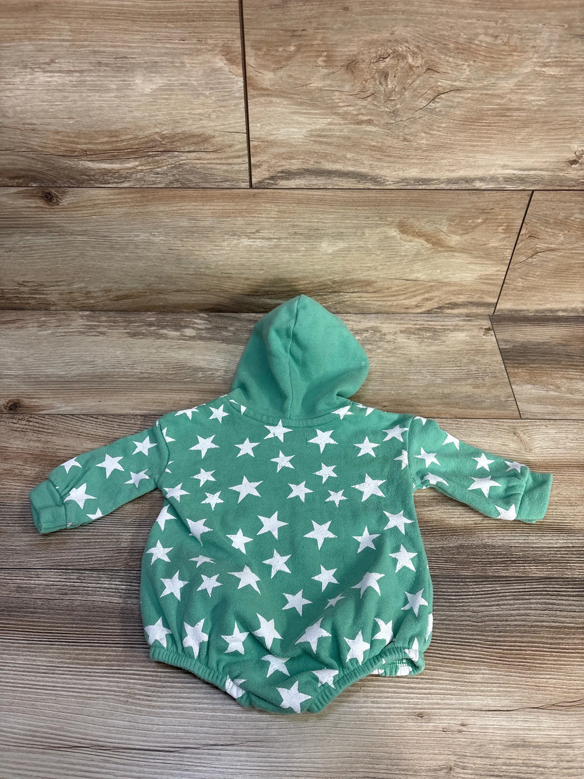 Back view of Grayson Mini hooded sweater romper showcasing green fabric, white star print, and hood on a wood floor
