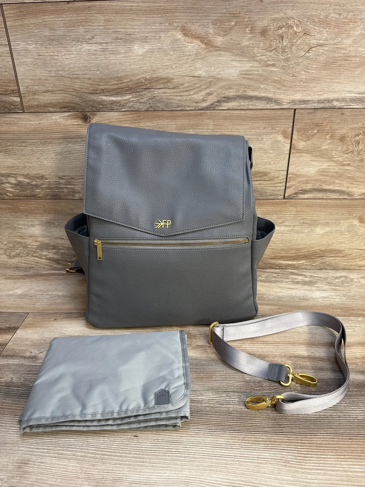 Front view of Freshly Picked Stone diaper bag; flap top, zip pocket, gold hardware, changing pad and strap