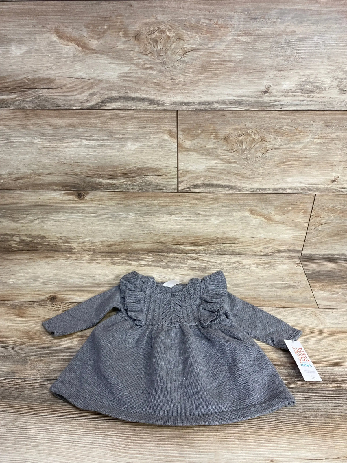 Front view of Just One You grey knitted dress (3M) with ruffle shoulders and cable-knit yoke on wood floor