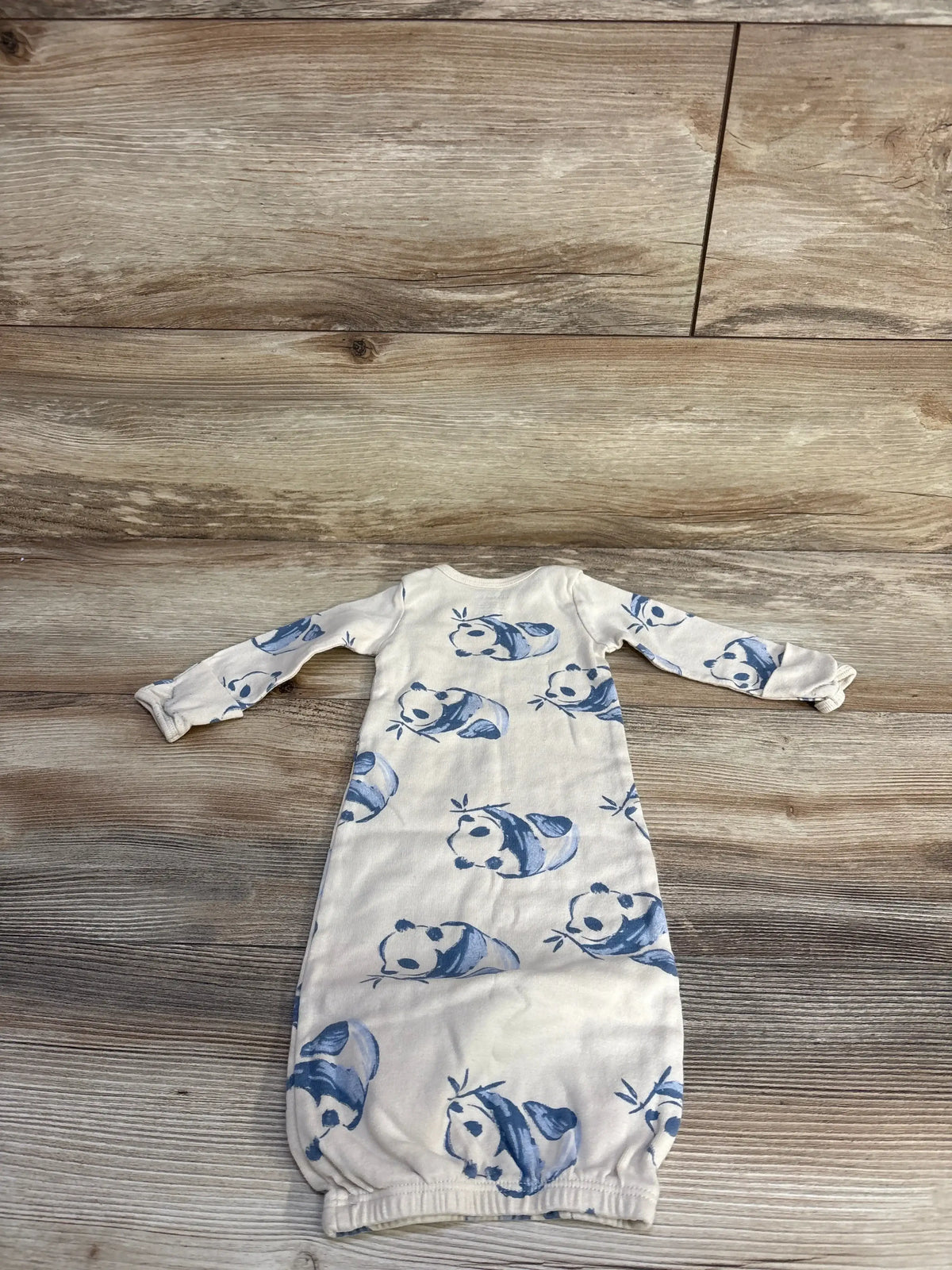 Flat lay of preemie beige Carter’s sleeper gown showing all-over blue panda print and elastic gathered bottom on wood floor background