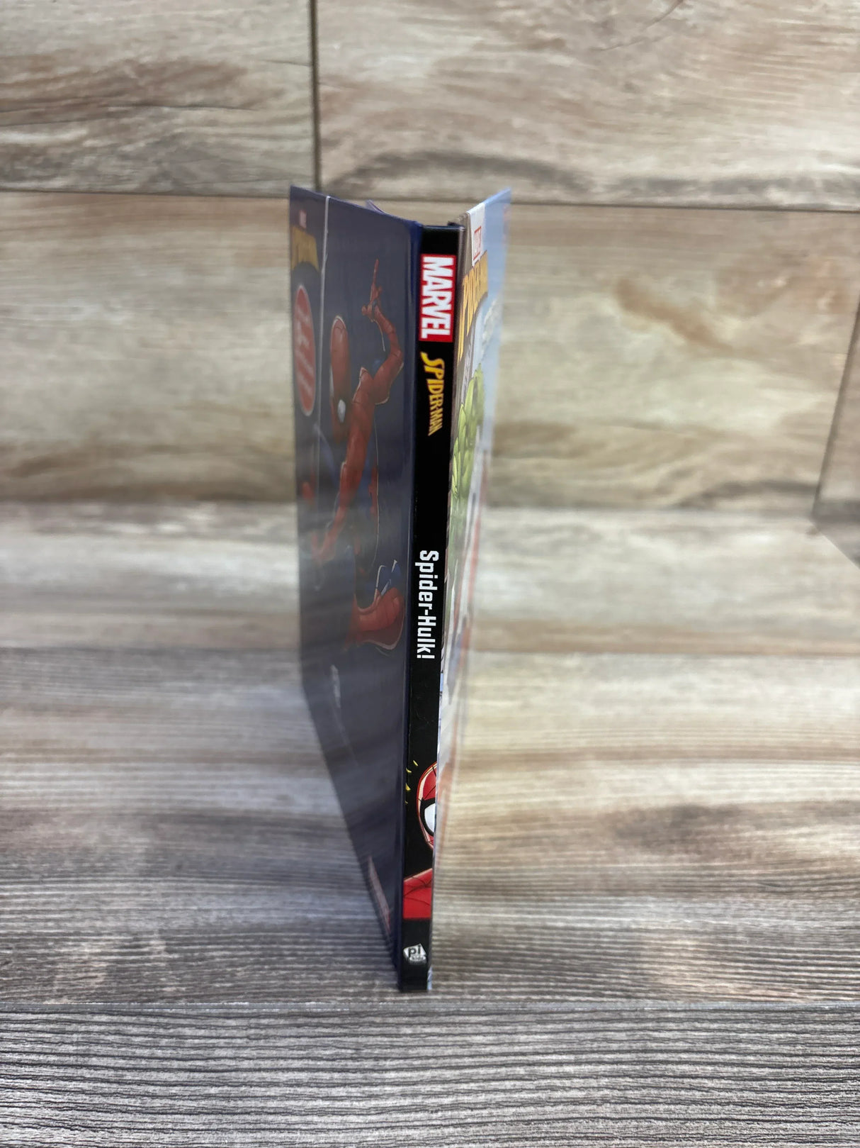 Side view of Marvel Spider-Man Spider-Hulk hardcover book showing spine with Marvel logo and title on a wooden surface