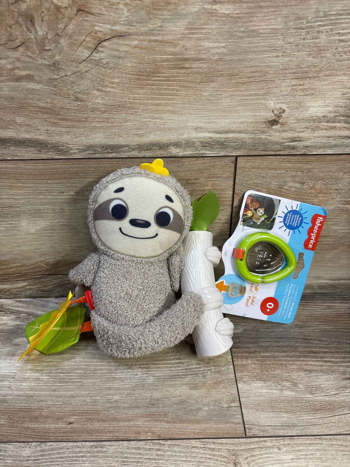 Front view of Fisher-Price stroller sloth plush holding a white tree-trunk teether and green leaf tag on wood background