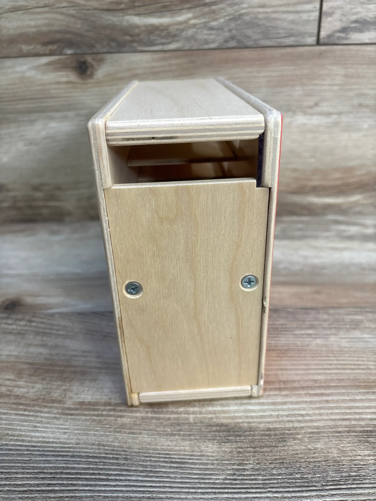 Front view of Lovevery Count and Slide Ring Chute showcasing hinged flap, screw details, and natural plywood finish on a wood plank floor