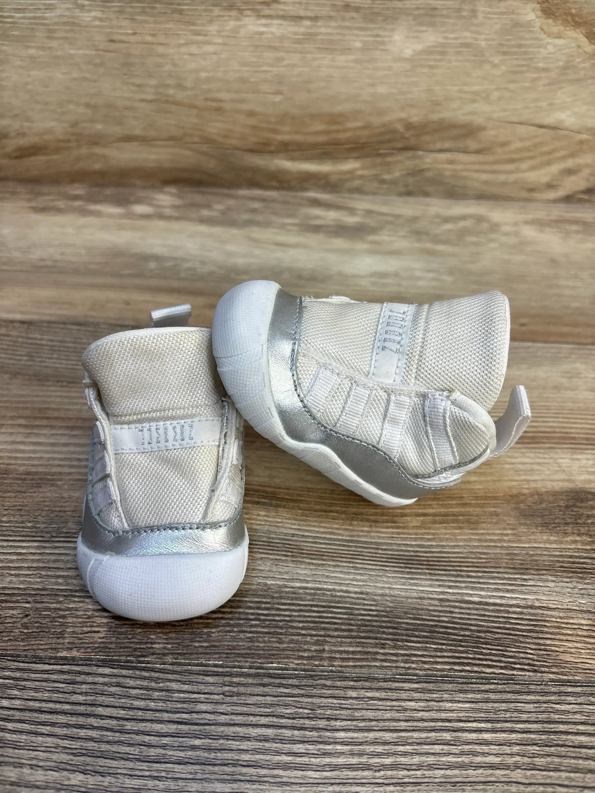 Front and side of Air Jordan 11 Retro TD toddler sneakers showcasing white mesh upper, metallic silver mudguard and white rubber soles on wood background