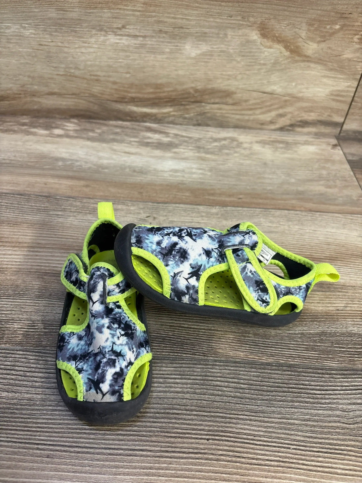 Angled view of OshKosh Aquatic Water Shoes in grey and green, size 7C, showcasing hook and loop closure on wood-grain flooring