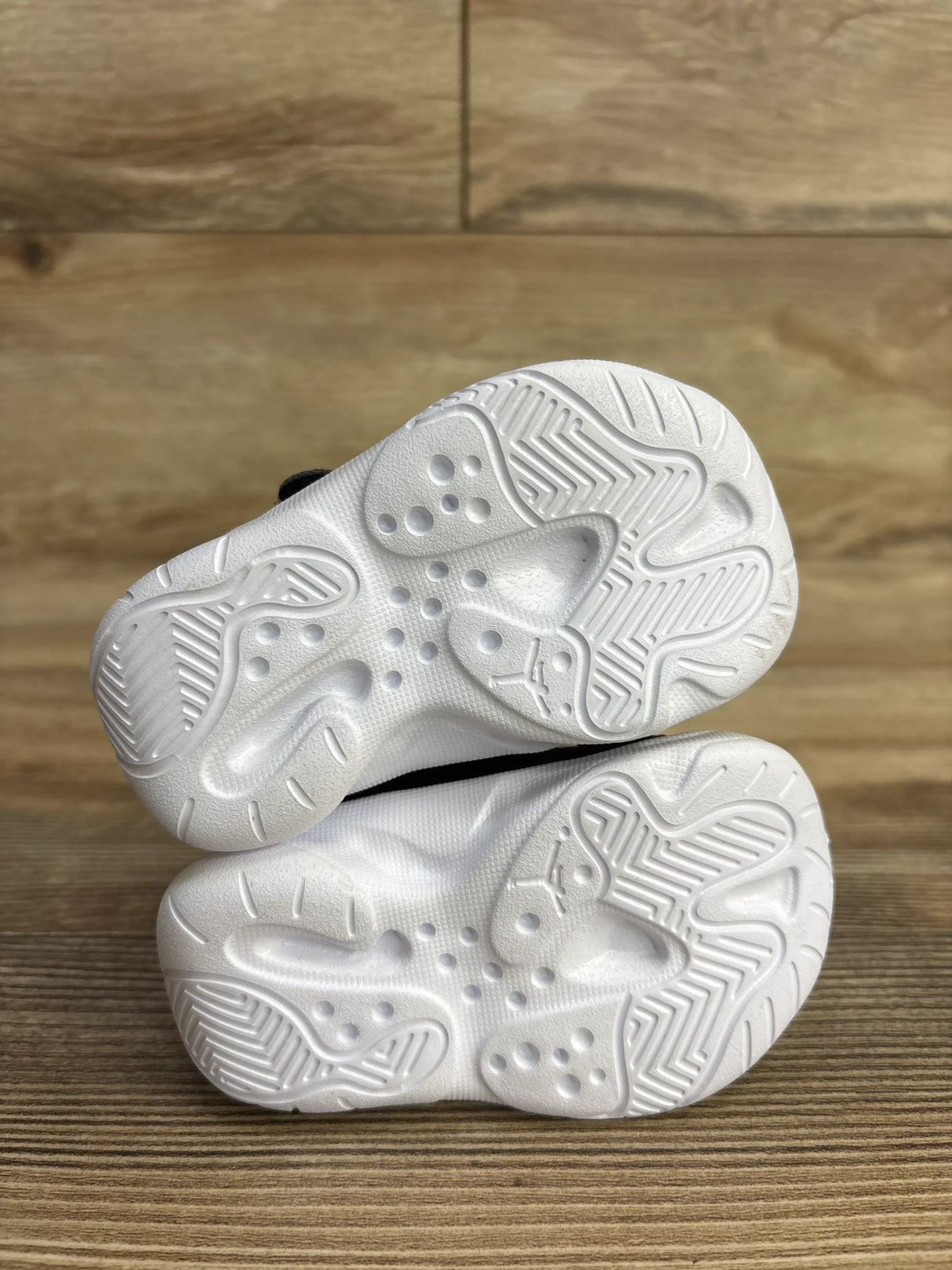 Close-up of Air Jordan 11 CMFT Low TD ‘Black Taxi’ toddler sneakers showing white textured rubber soles on wood floor