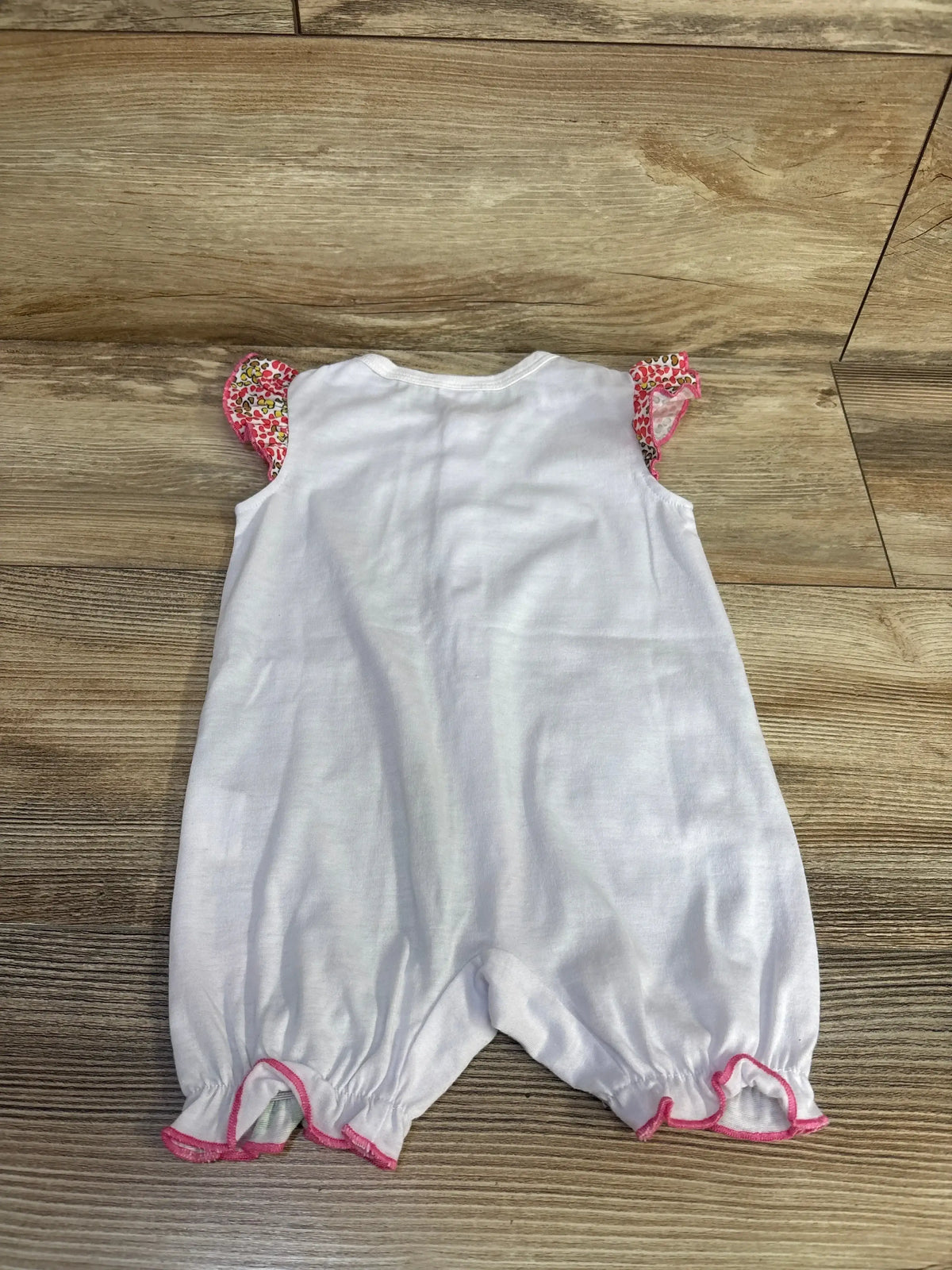 Back view of white baby romper showing pink ruffled cap sleeves with floral trim and pink ruffled leg openings on wood floor