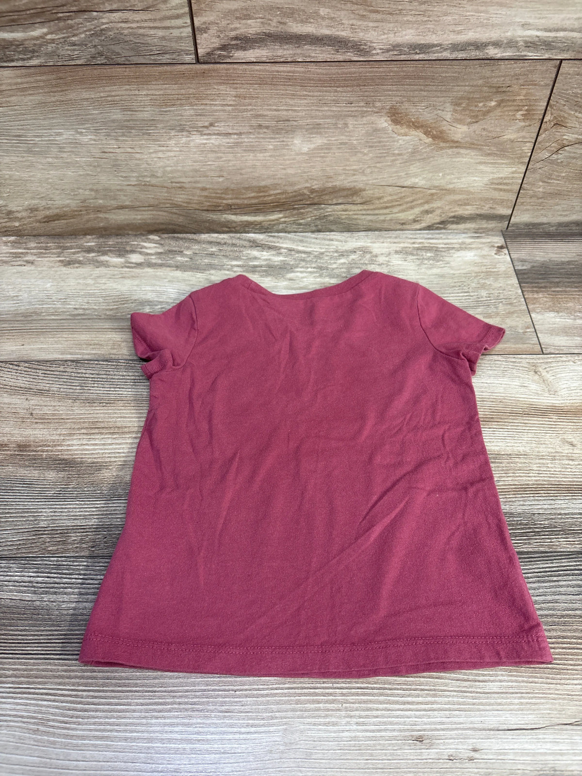 Back view of Oshkosh Radiate Love shirt in pink, size 3T, showing short sleeves and plain back on a wood surface