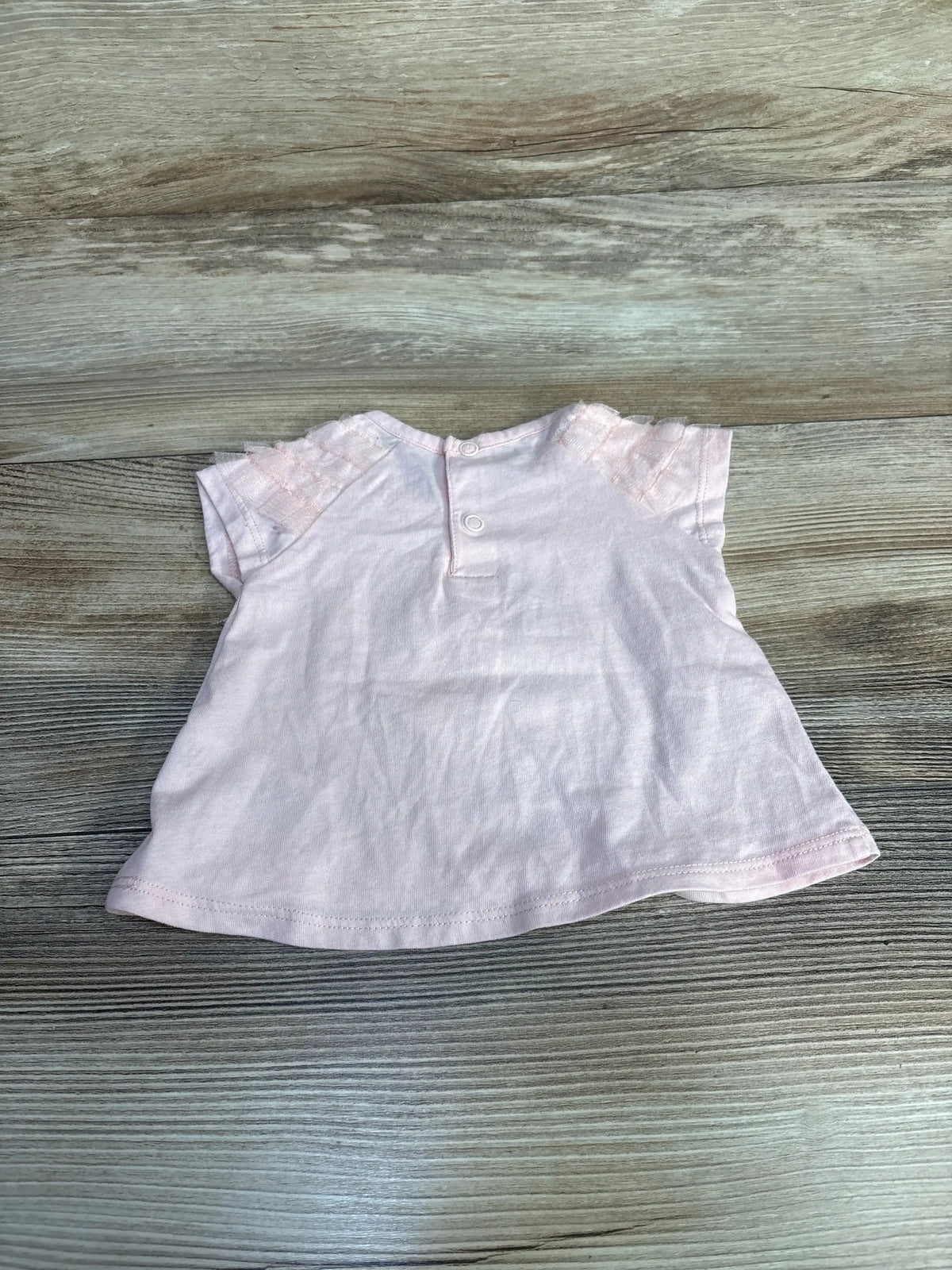 Flat-lay back of Disney Baby Minnie Mouse pink 3-6m shirt showing two-button closure and lace cap sleeves on wood