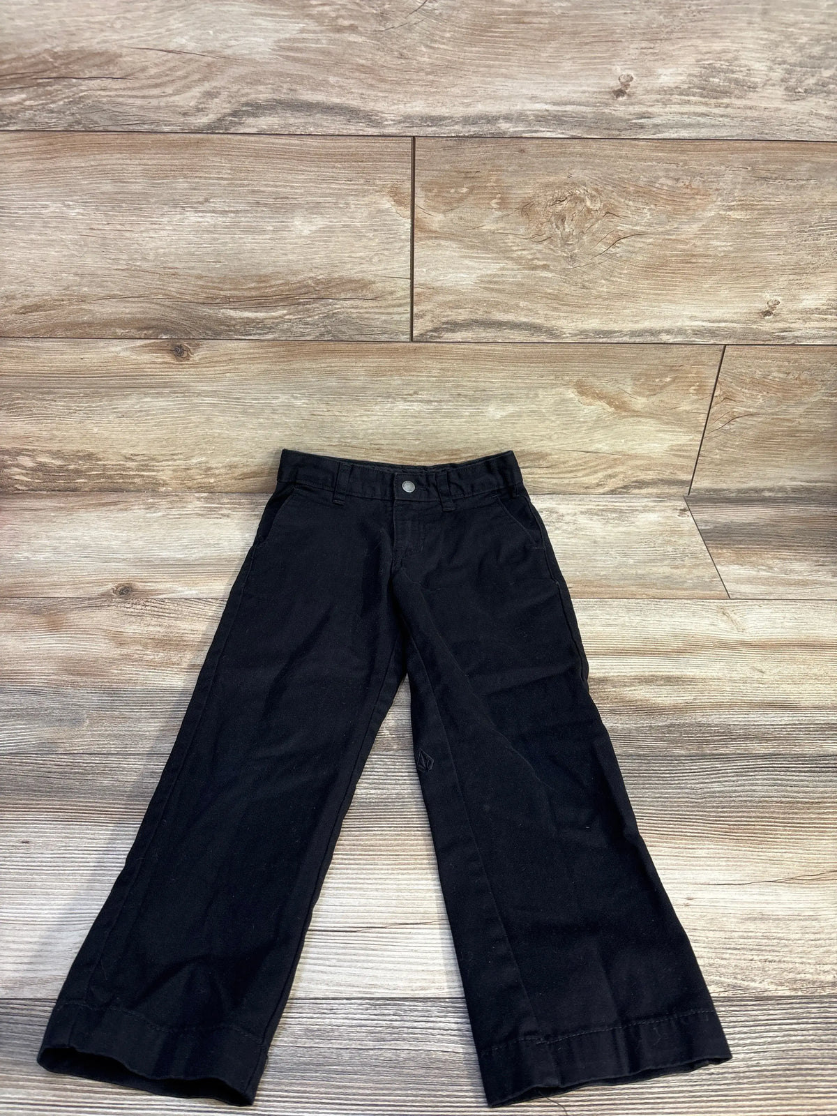 Flat lay of Volcom VMonty toddler black pants showing straight legs, front pockets, and button waist on light wood floor