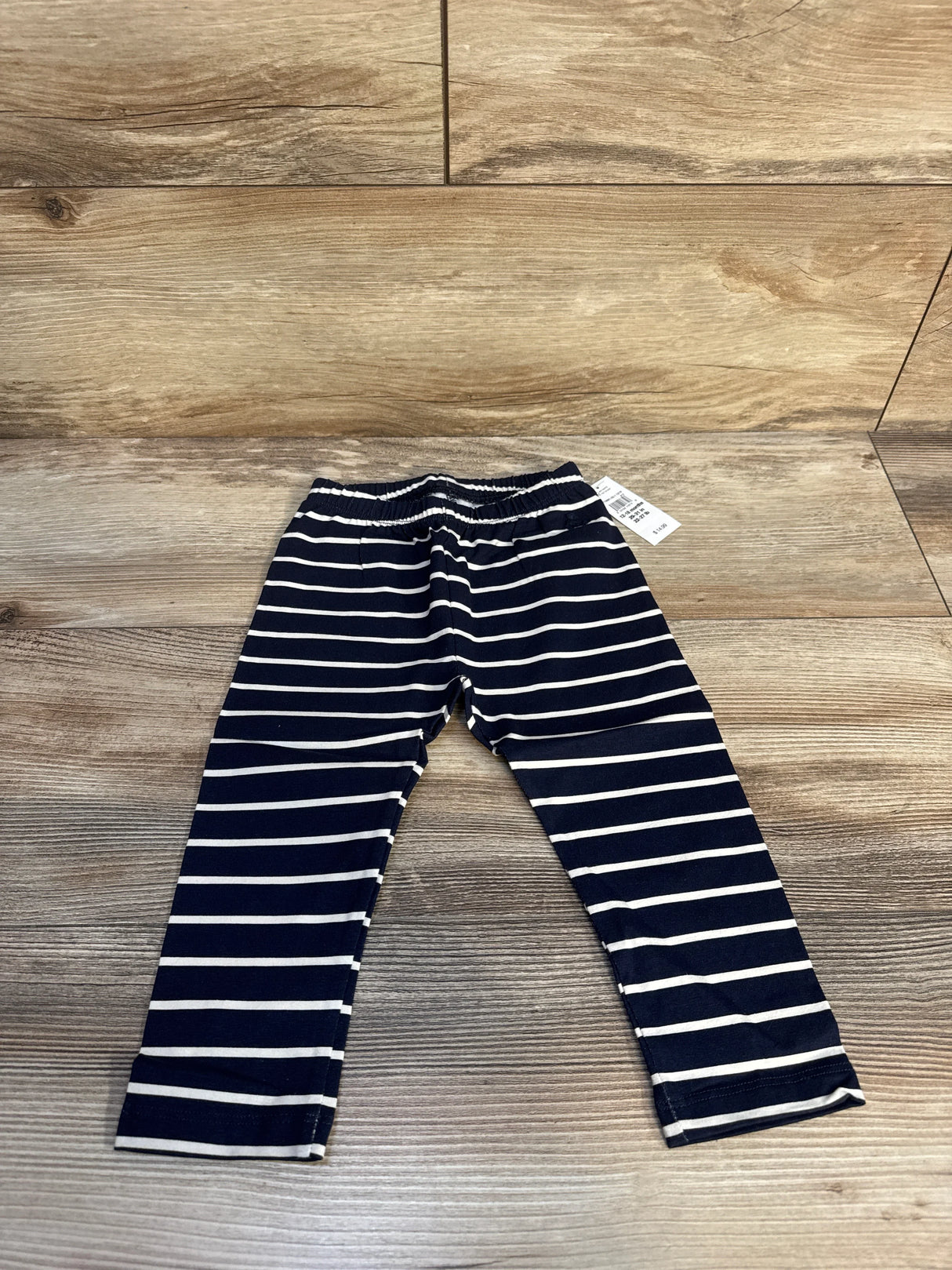 Navy blue and white striped baby leggings on wood floor with price tag visible
