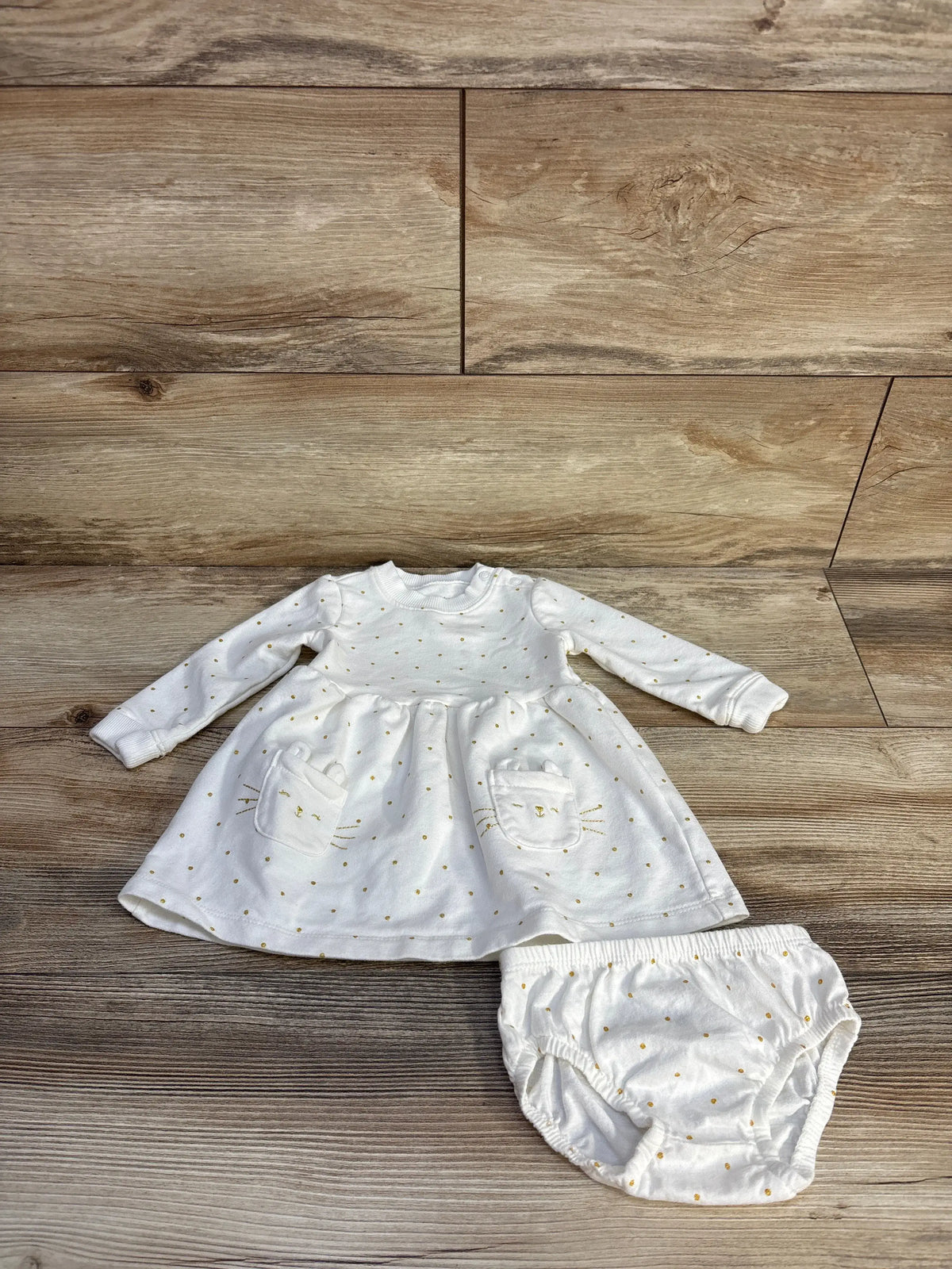Flat lay of Carter’s white polka dot sweatshirt dress and bloomers set showcasing long sleeves on a wood floor